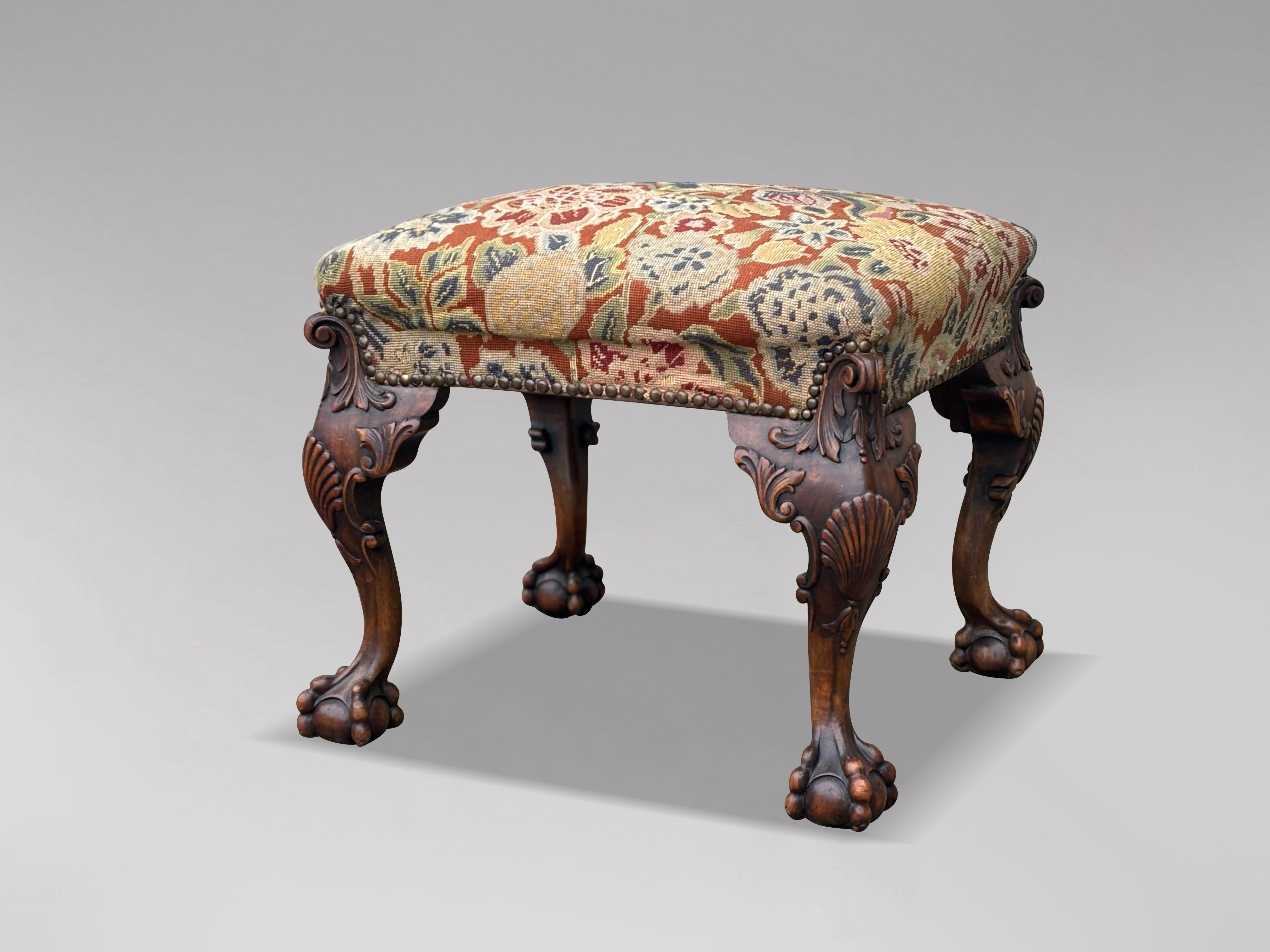 An early 19th century, Regency period carved walnut and needlework foot stool, retaining excellent colour and patina. Featuring a rectangular petit-point floral needlework upholstered seat above a shaped and scrolled foliate-edged seat frame and