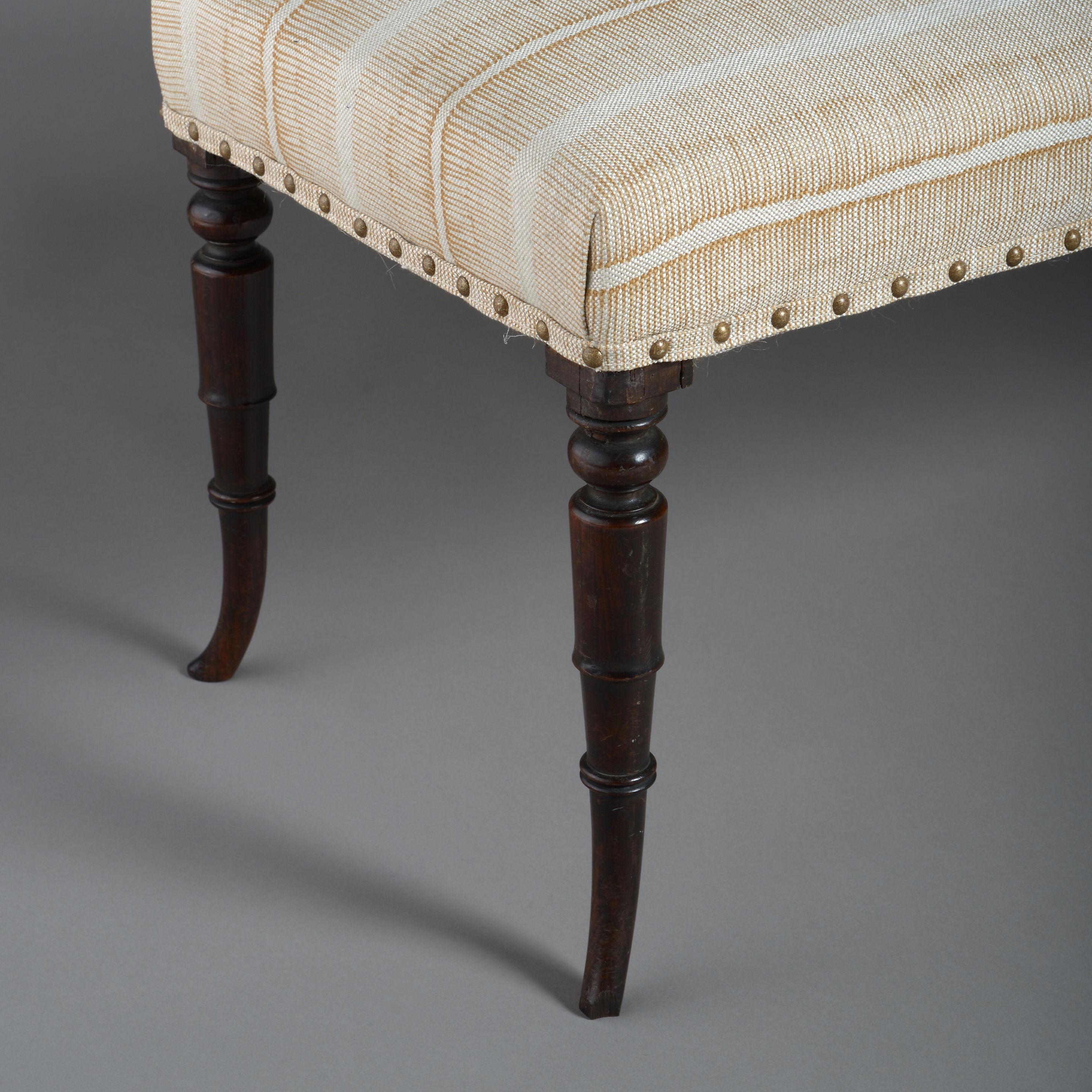 An early 19th century Regency Period upholstered long stool, the upholstered seat set upon four turned mahogany sabre legs.