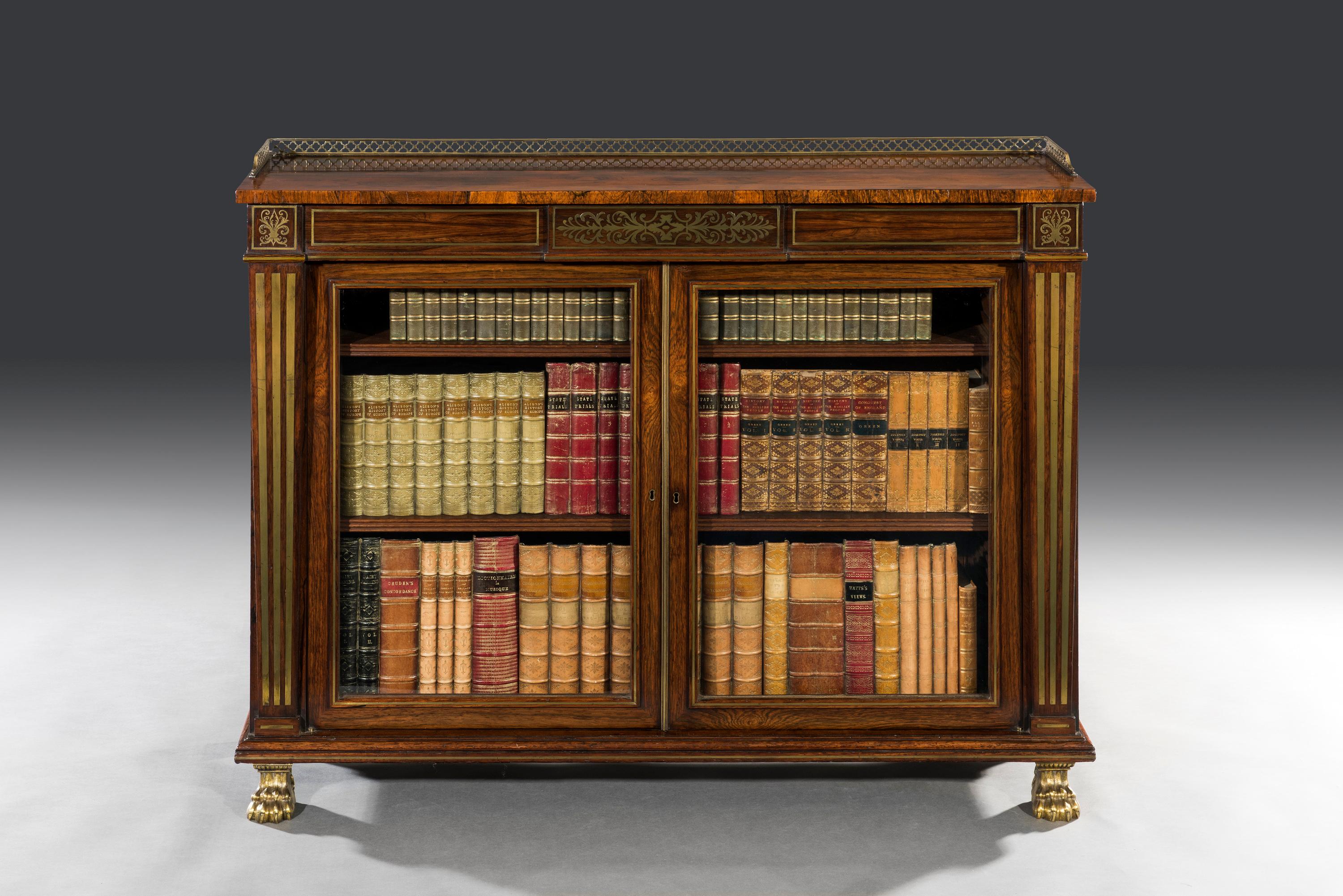The highly figured brass-mounted rosewood rectangular top above a brass inlaid and brass strung frieze sits above glazed rosewood brass strung doors and flanked by brass fluted inlaid capitals. The glazed bookcase stands on its original feet with