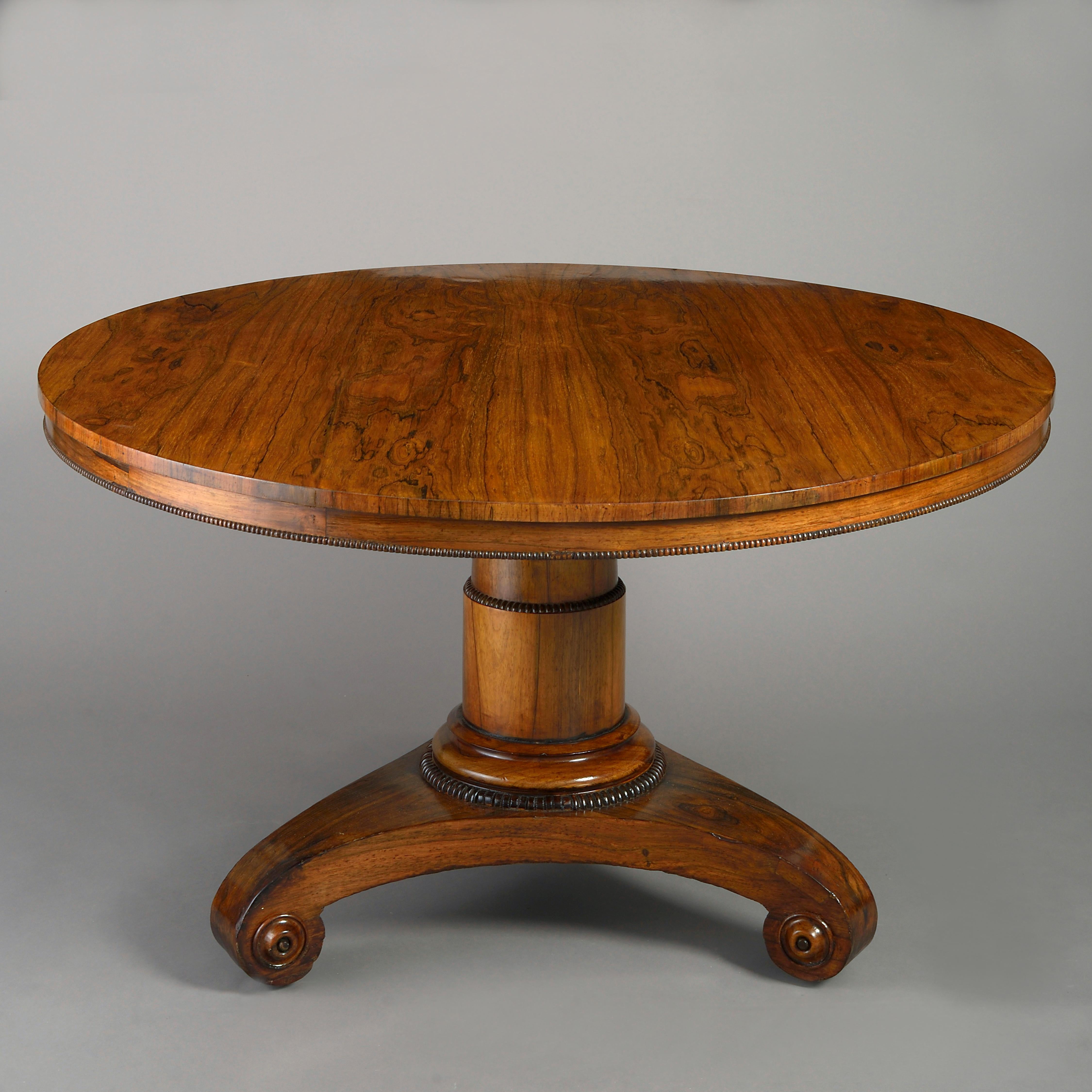 An early 19th century Regency Period rosewood centre table or breakfast table, the finely figured circular walnut veneered top with beaded apron, set upon a gun barrel stem and raised on a shaped concave triform base with roundels and the original