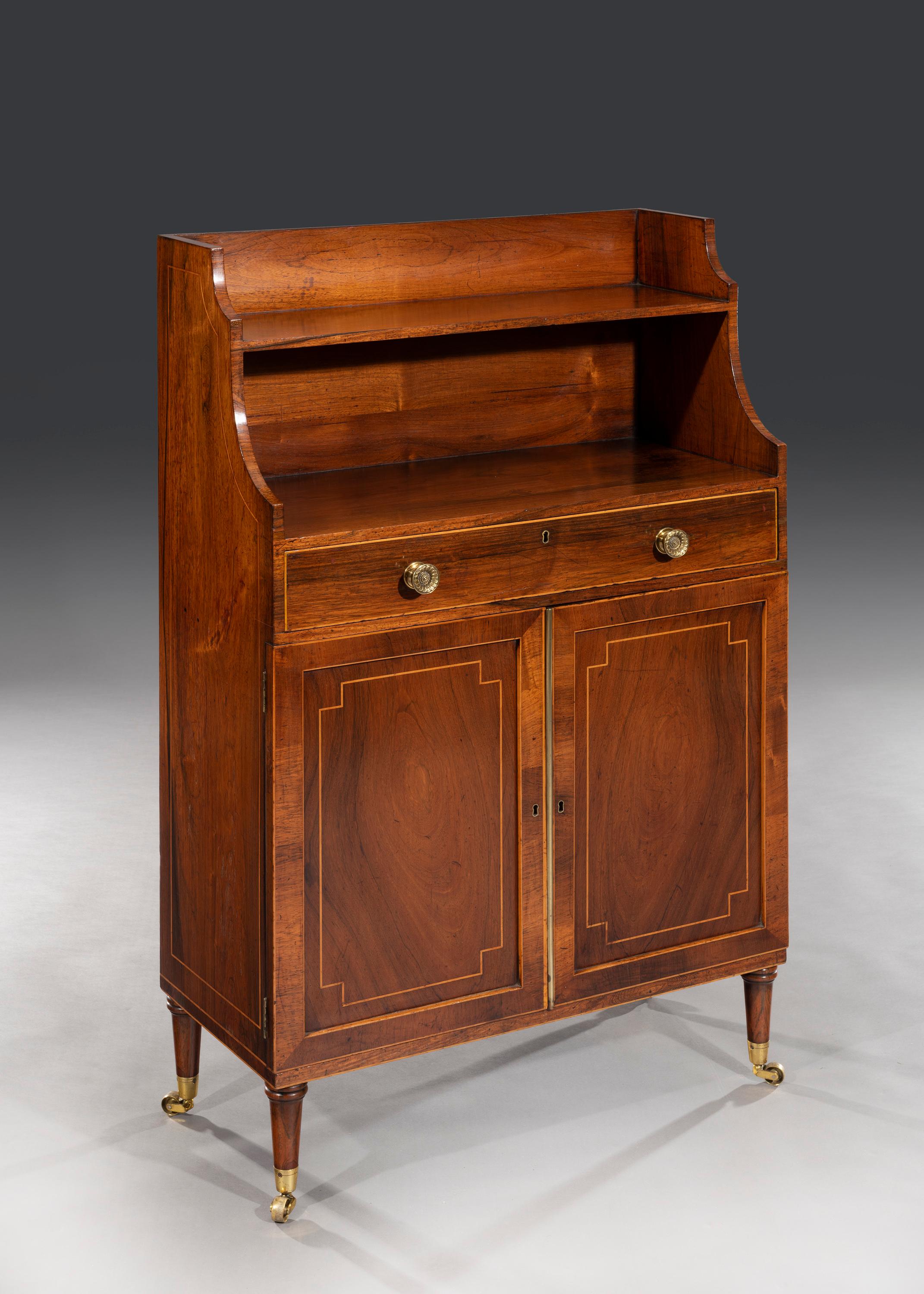 The rosewood veneered waterfall bookcase sits above a single full length drawer with brass handles. The drawer lining is mahogany and the cupboard doors are inset with 