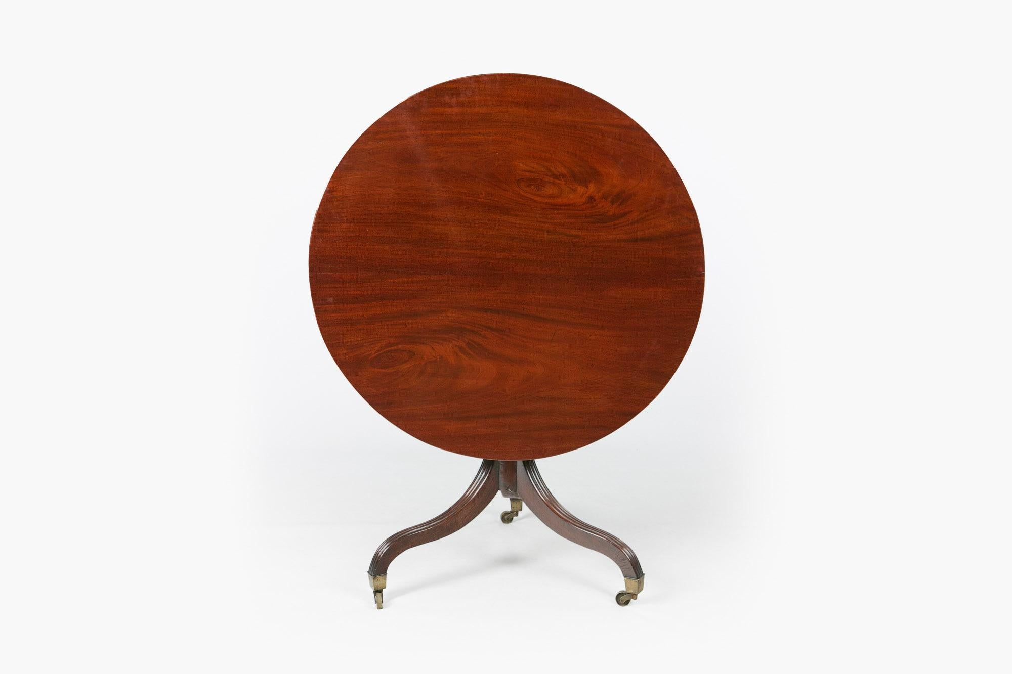 Early 19th century Regency mahogany tip up breakfast table, the moulded top of circular form with reeded edge raised over ring turned column pod supported on three outswept scrolling reeded legs terminating on brass caps and casters.