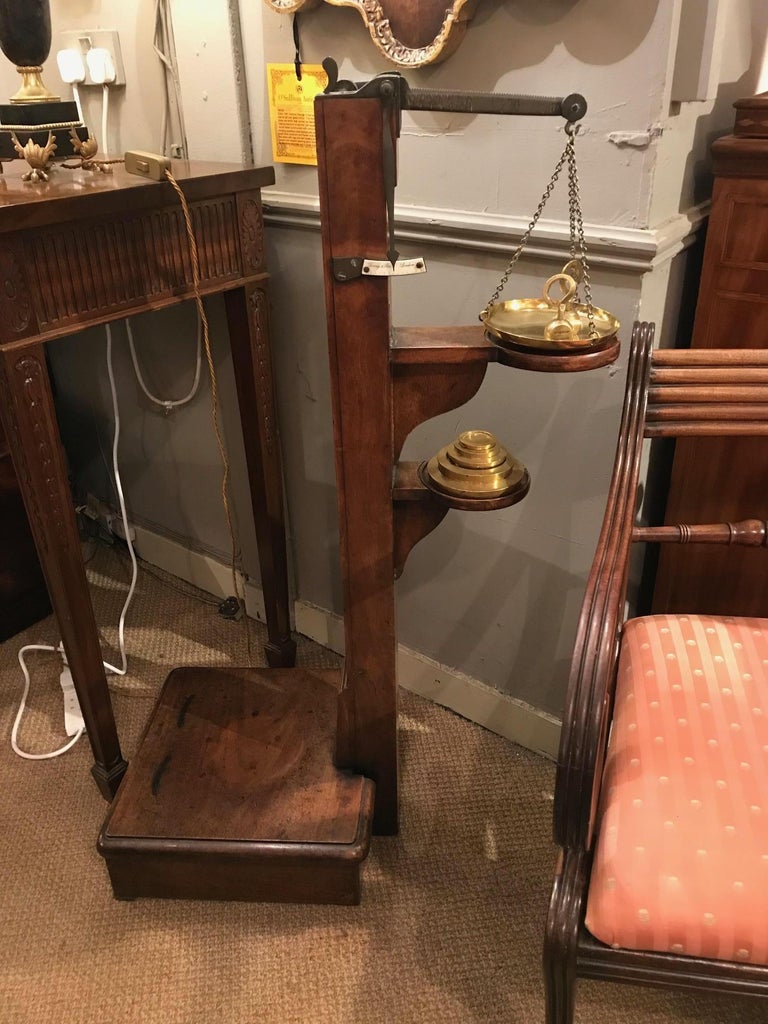 Early 19th century Regency mahogany weighing scales, the central support with concealed height measuring stick, measurement scale and brass weighing scale raised over two moulded shelves of circular form holding scale and brass measuring weights