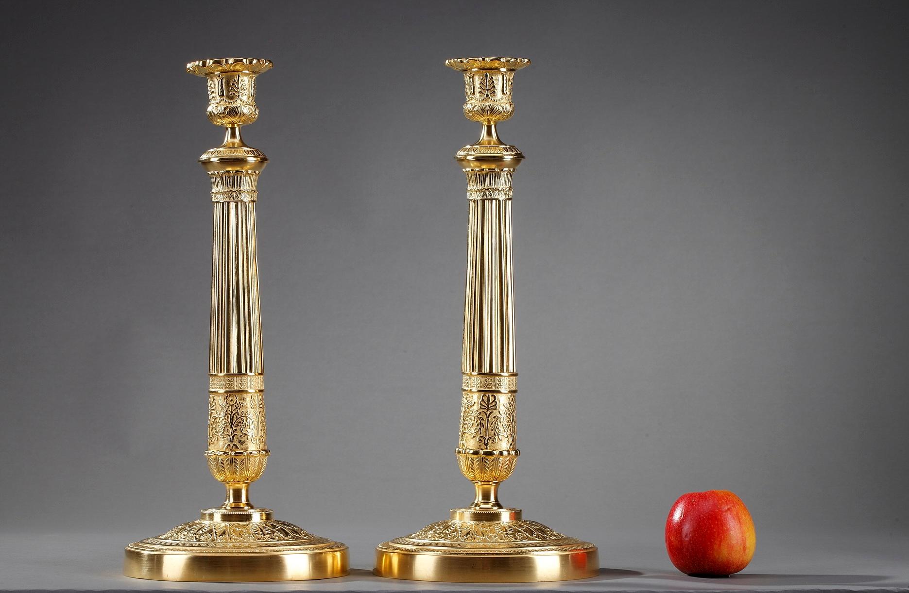 Large French restauration ormolu candlesticks. Crafted of gilt bronze, the pair feature a finely chiseled scrolling foliage and acanthus leaf motif. The sockets are embellished with palmette and floral motif. The fluted stems are supported by a