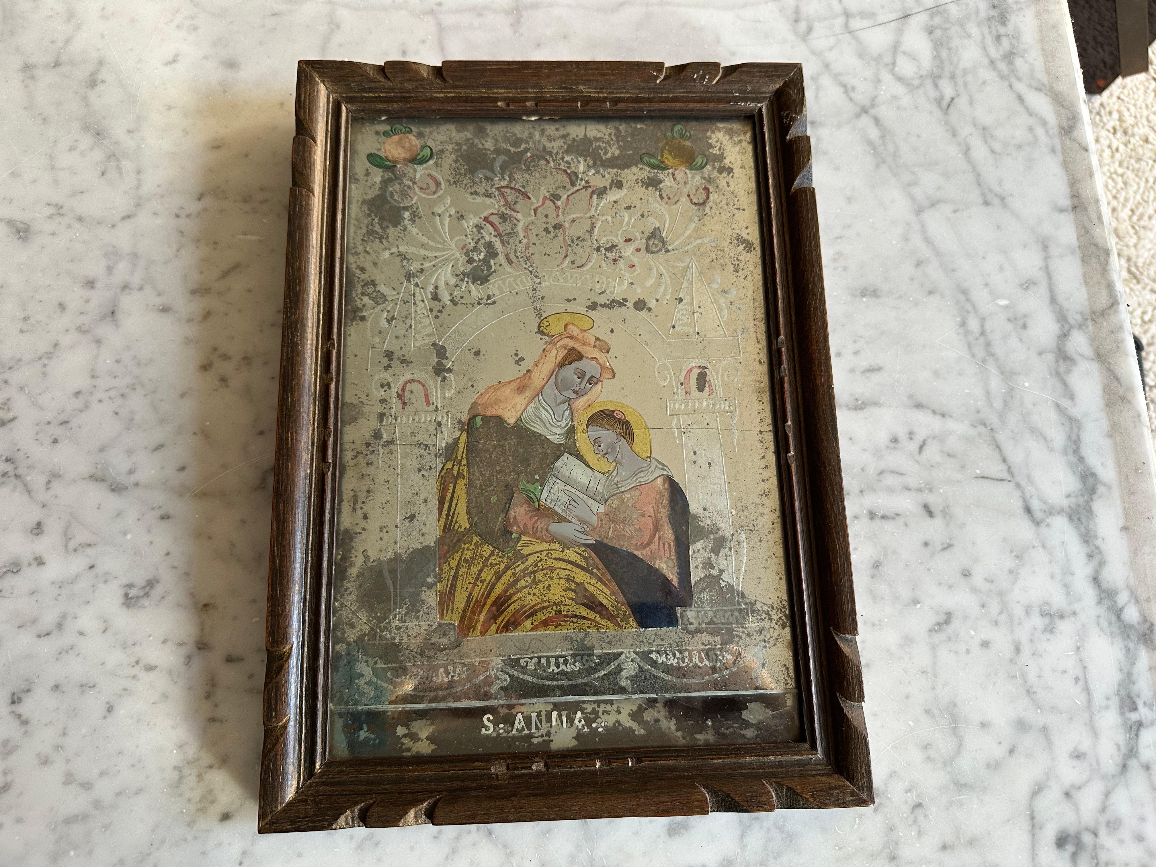 This exquisite reverse glass painting from the early 19th century features Saint Anne, a revered figure in Christian tradition, known as the mother of the Virgin Mary and patron saint of mothers, teachers, and women in labor. Her depiction in art