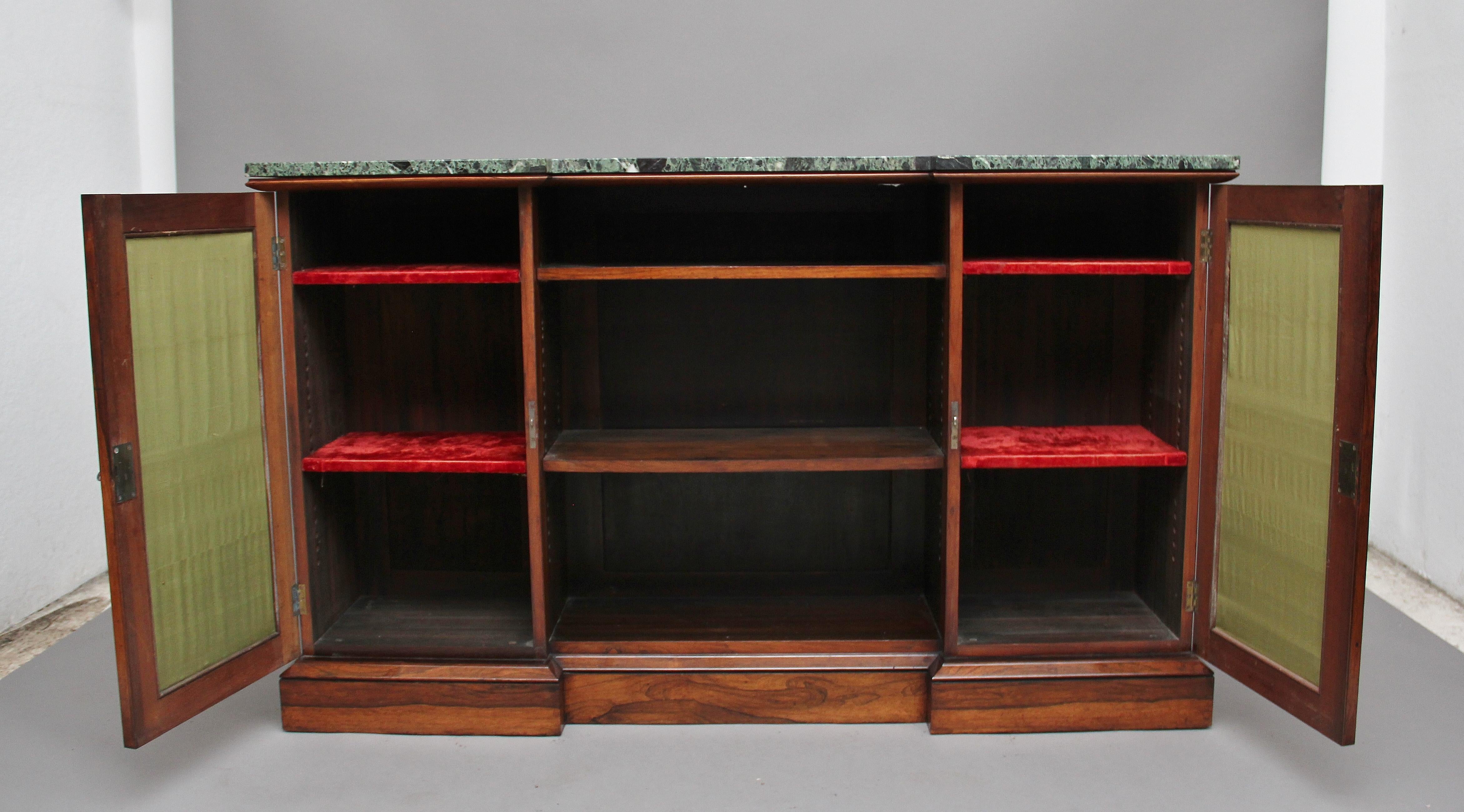 Early 19th century rosewood inverted breakfront side cabinet, having a green marble top above a central open compartment with two adjustable shelves, flanked by two pleated fabric panel doors opening to reveal two shelves, raised on a plinth base.
