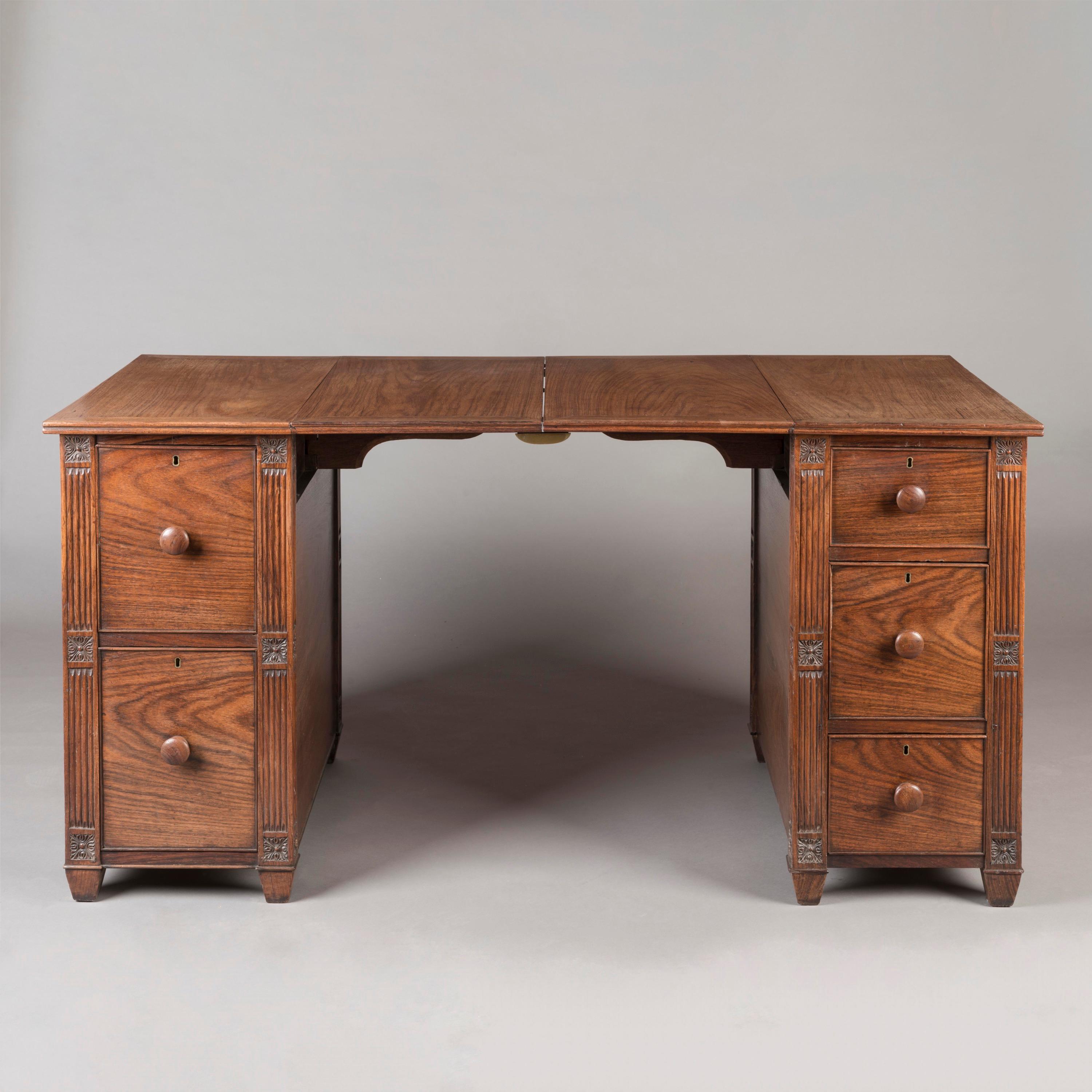 An Ingenious 'Collapsible' Campaign Pedestal Desk

Constructed from rosewood, each pedestal supported on tapering feet, one enclosing two drawers and the other a bank of three drawers, all lockable and with turned knobs, the angles finished as