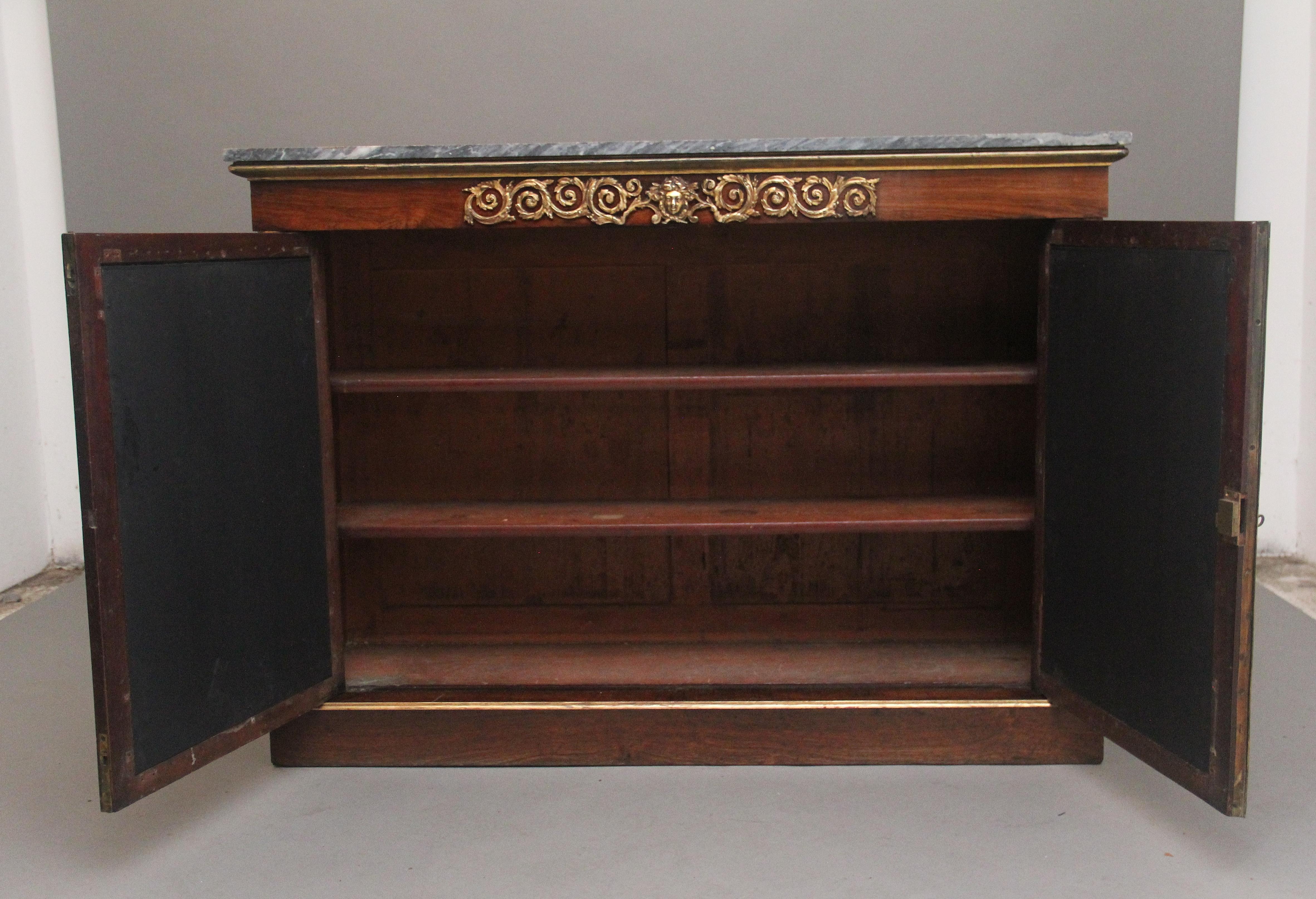 A fabulous quality early 19th Century rosewood, gilt and marble top cabinet, having the original veined grey marble top above a frieze with a highly decorative pierced and carved ormolu mount with figure head at the centre, two cupboard doors below