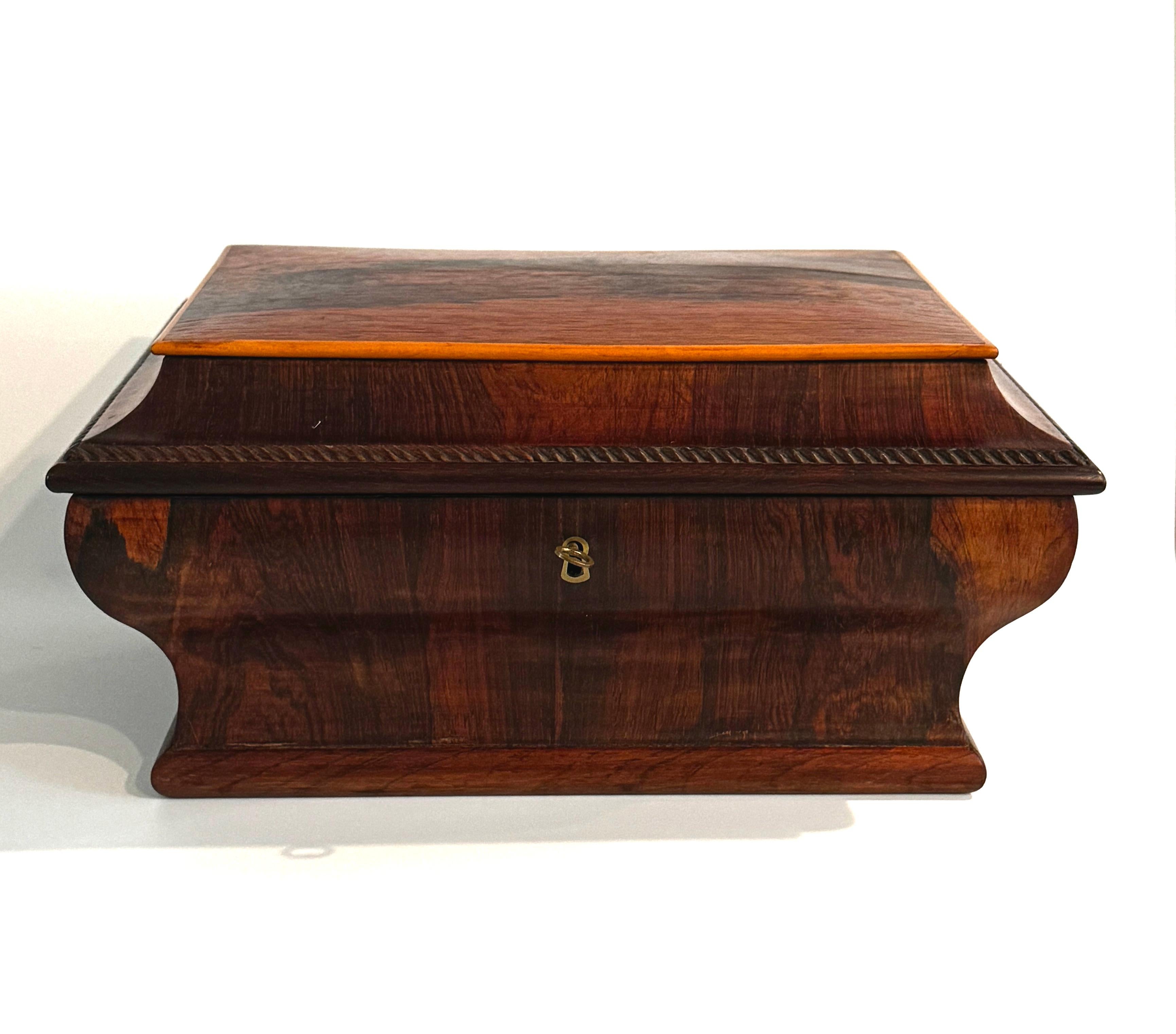 Scatola da cucito in palissandro dell'inizio del XIX secolo. Questo bellissimo e grande cofanetto ha un'eleganza semplice, con la sua forma a bombe, a sarcofago e il suo legno di palissandro splendidamente venato. L'esterno è decorato con un bordo a
