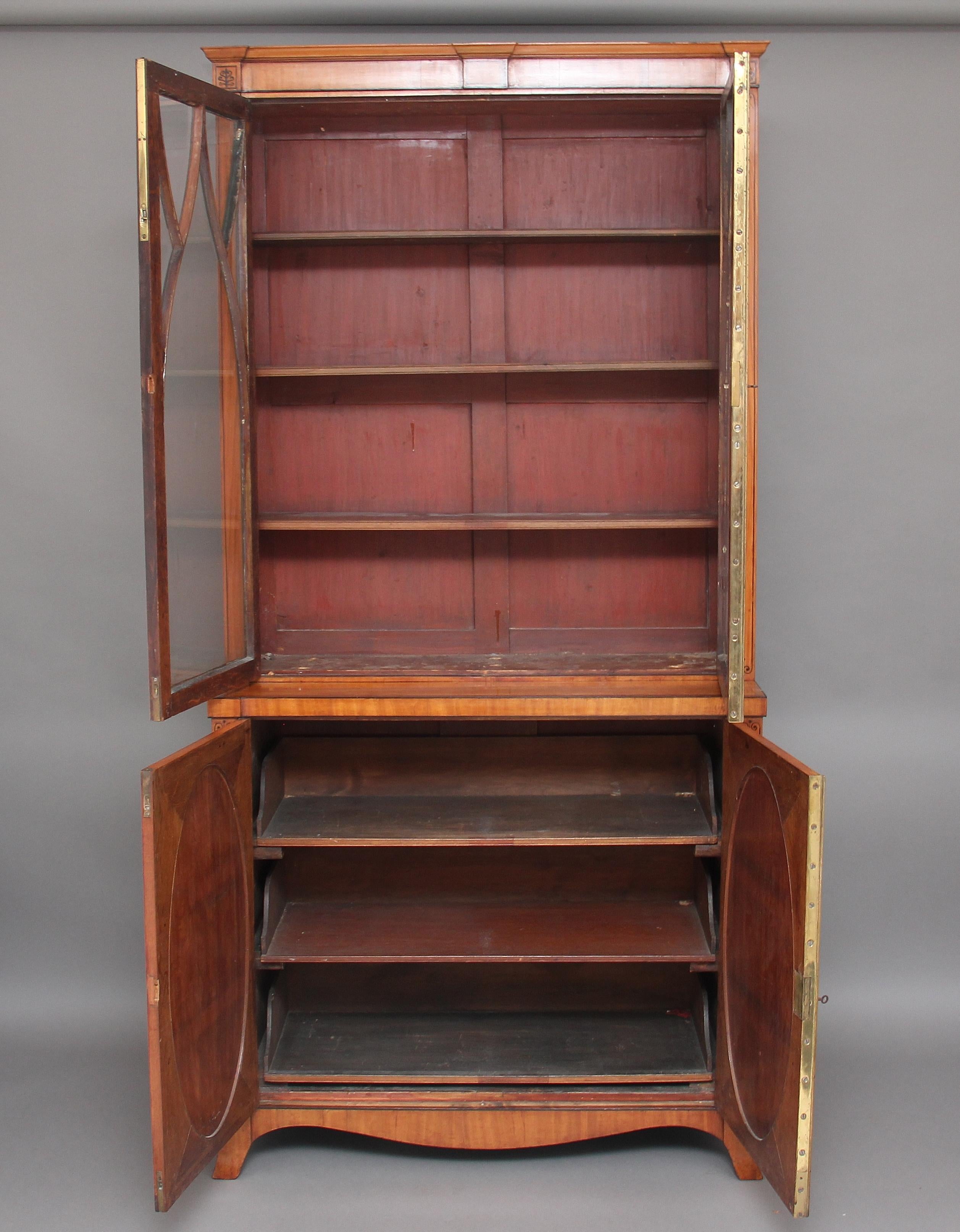 Early 19th century satinwood bookcase, having a nice elegant cornice decorated with ebony inlay above two glazed doors with Gothic glazing bars, opening to reveal three shelves inside, the bottom section having two oval panelled doors opening to