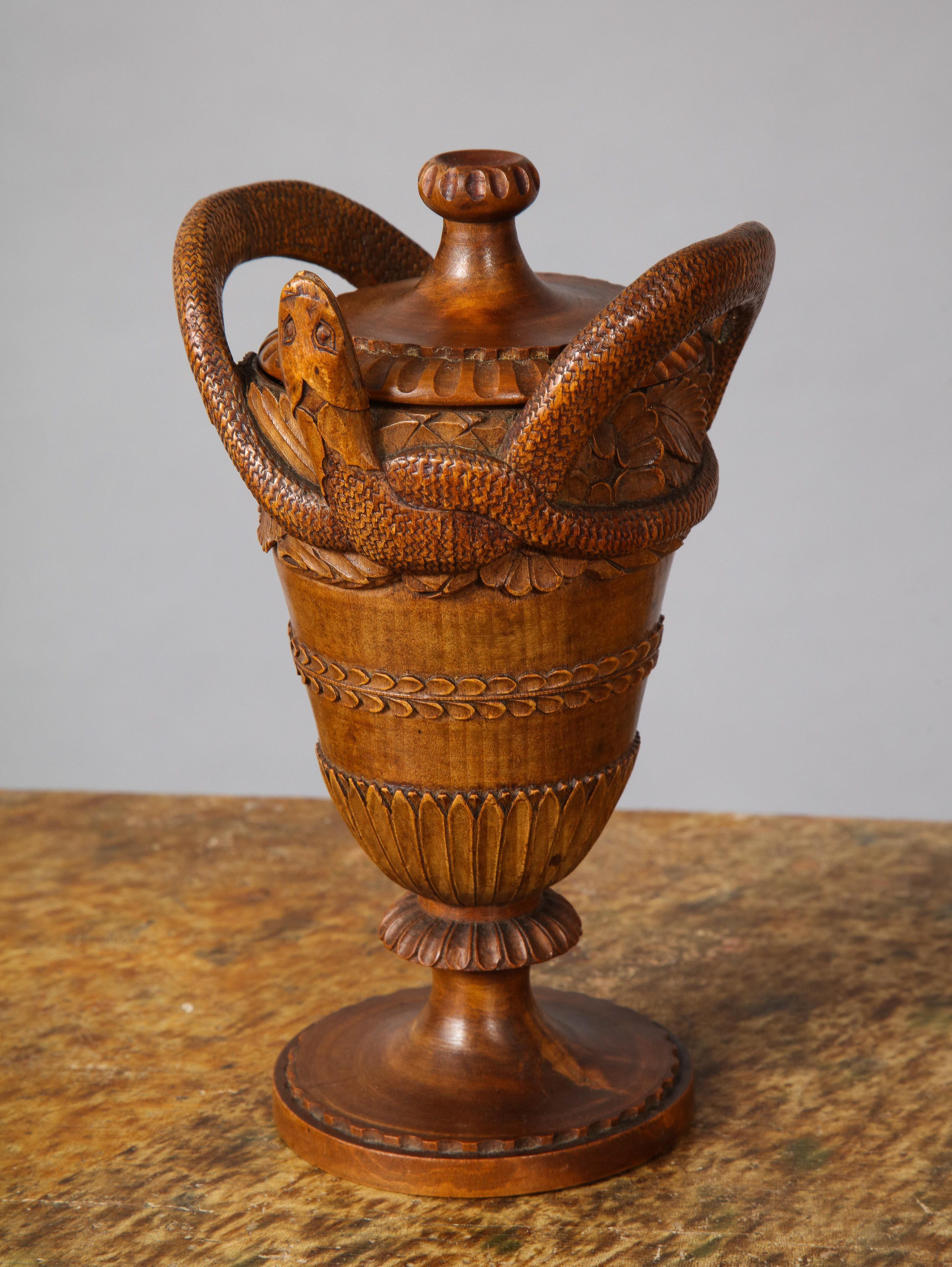 Very fine early 19th century carved wood neoclassical urn with gadrooned finial and entwined snake handles, tapered base with long leaf carving and standing on turned base, the whole with good rich color and patina.

  