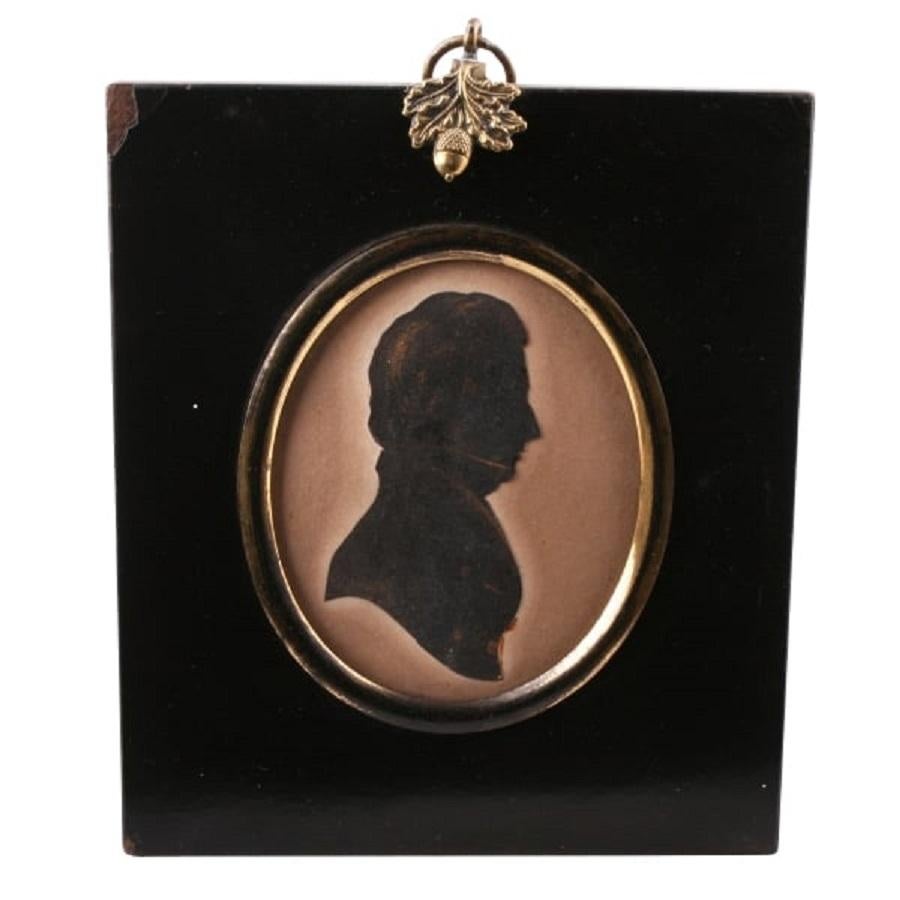 An early 19th century Regency period silhouette of a Gentleman.

The silhouette is fitted in a gilded brass oval frame with a domed glass cover and is held in a black lacquered oblong frame.

The frame hangs from a gilded brass ring that has an