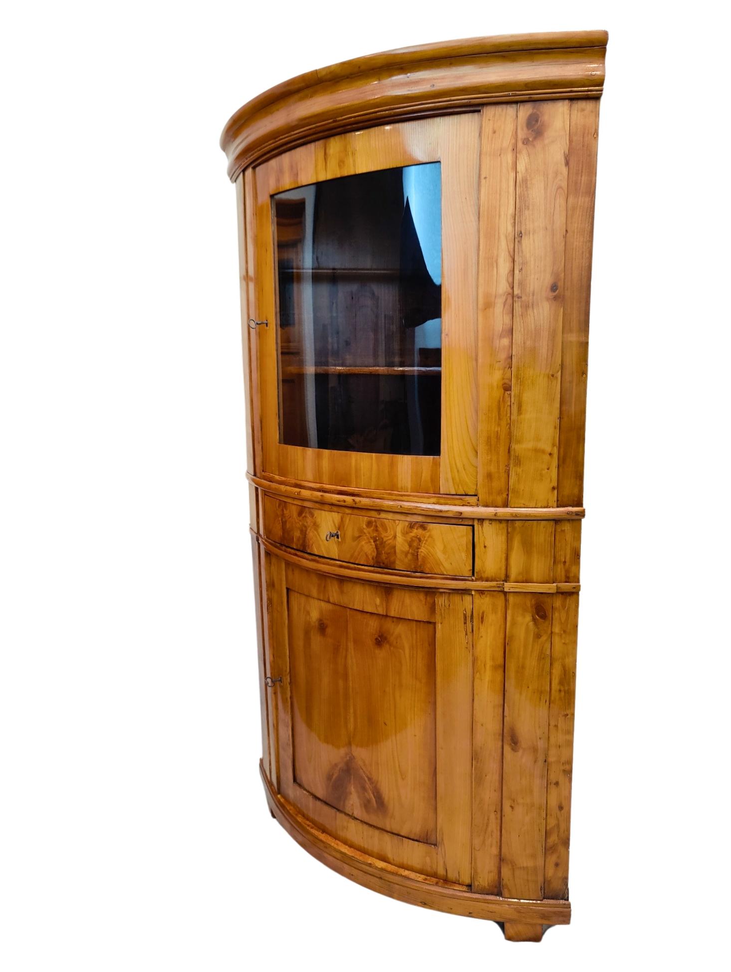 Questo raffinato mobile angolare in legno di ciliegio Biedermeier è un classico esempio di artigianato del XIX secolo, che unisce eleganza e design funzionale. Realizzato in caldo legno di ciliegio con una splendida patina, questo mobile è stato
