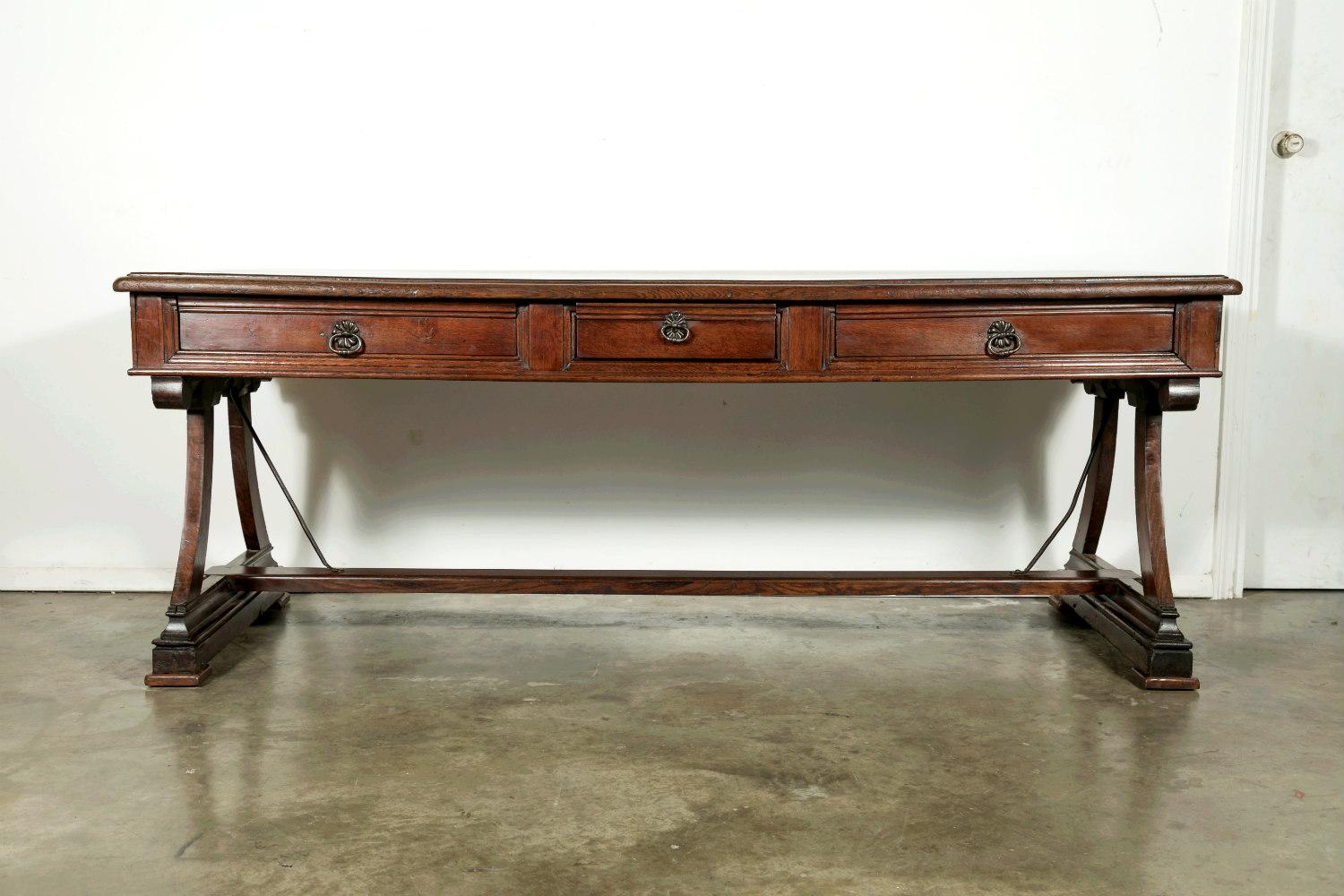 A handsome solid oak writing table from Provence, finished on all sides so that it can float in a room, circa early 1800s. Rectangular, beveled edge top with three carved drawers across the front and carved frieze on the back. Raised on a pair of