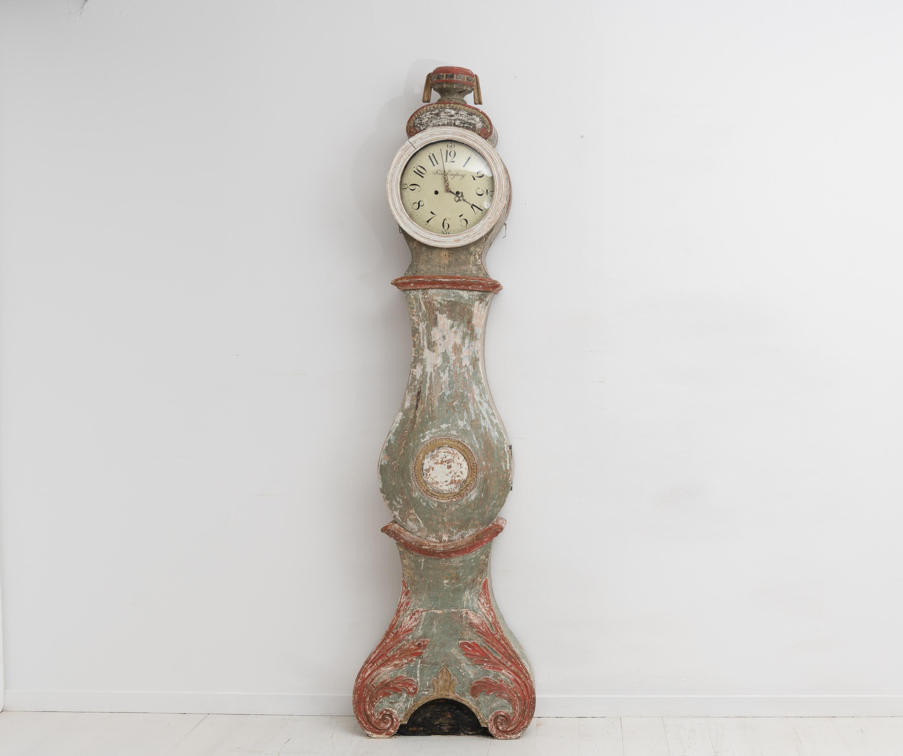 Southern Swedish long case clock from the early 1800s in rococo style. The clock is hand-made from pine with original hand-craved decor. Dry scraped to traces of the original green, red and gold paint. The curved shape typical for the rococo period