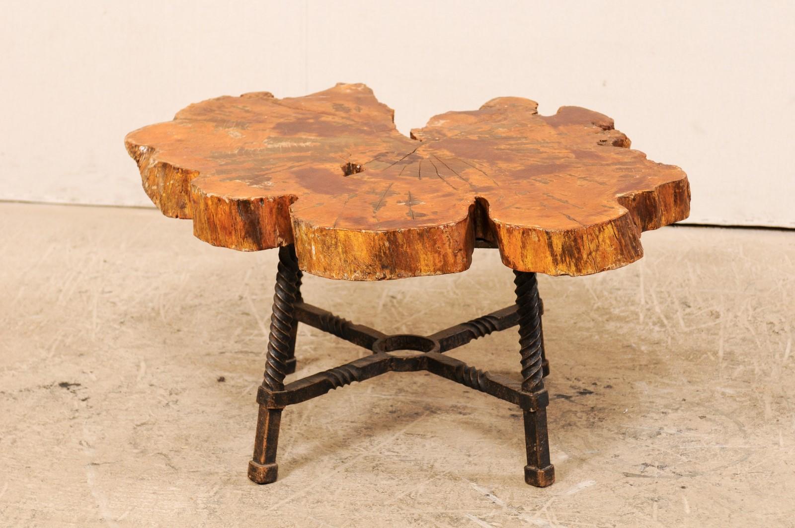 An early 19th century Spanish coffee table with wood slab top and fabulous forged iron base. This deliciously rustic coffee tables features a live-edge wood slab top, organic in shaped, which rests atop a hand forged iron base comprised of four