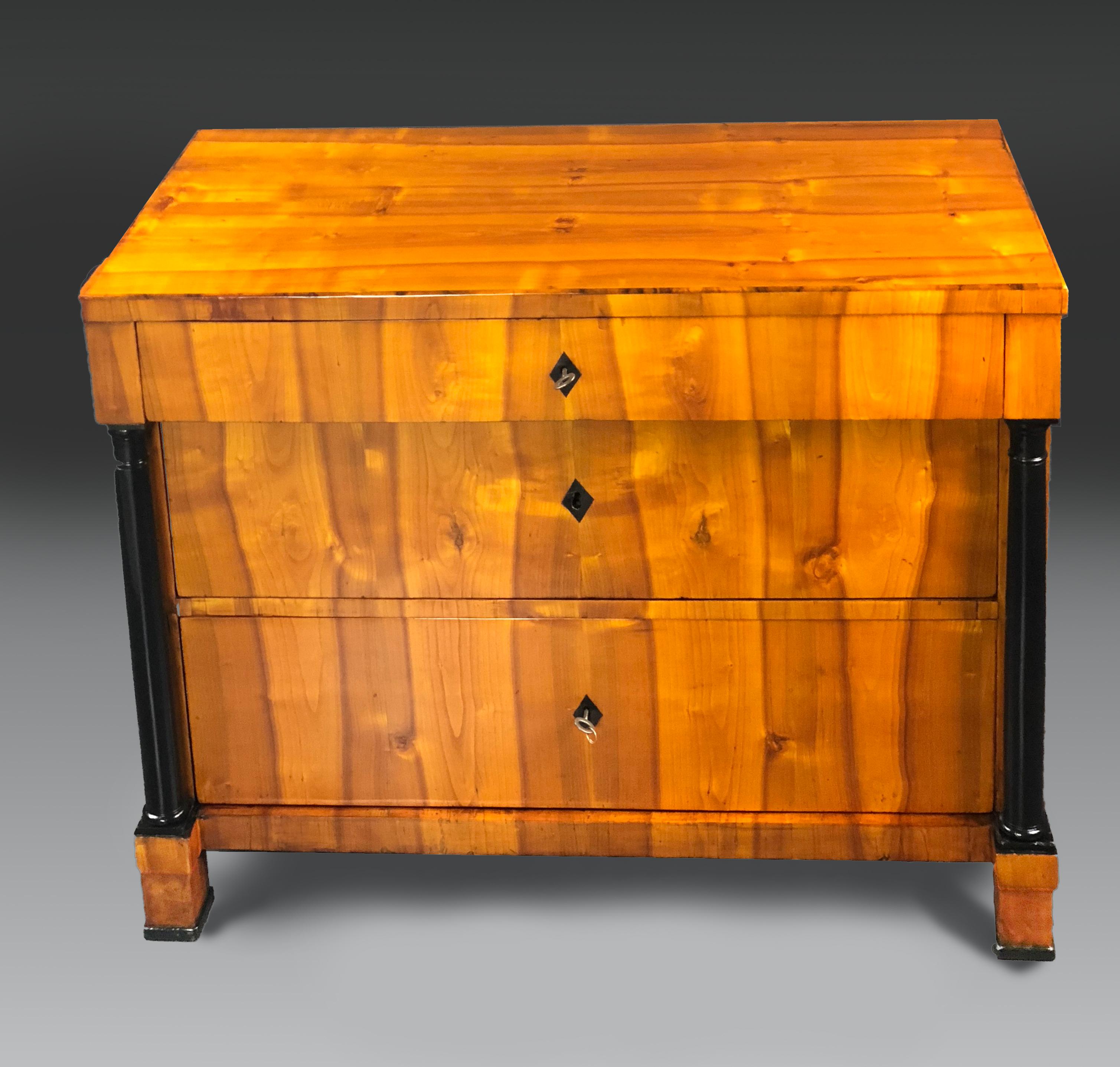 Early 19th century Biedermeier commode with beautifully matched cherrywood veneers of Swedish origin. One small drawer above 2 large ones flanked by black lacquered Doric style columns. All drawers have rhomboid shaped buffalo Horn keyhole