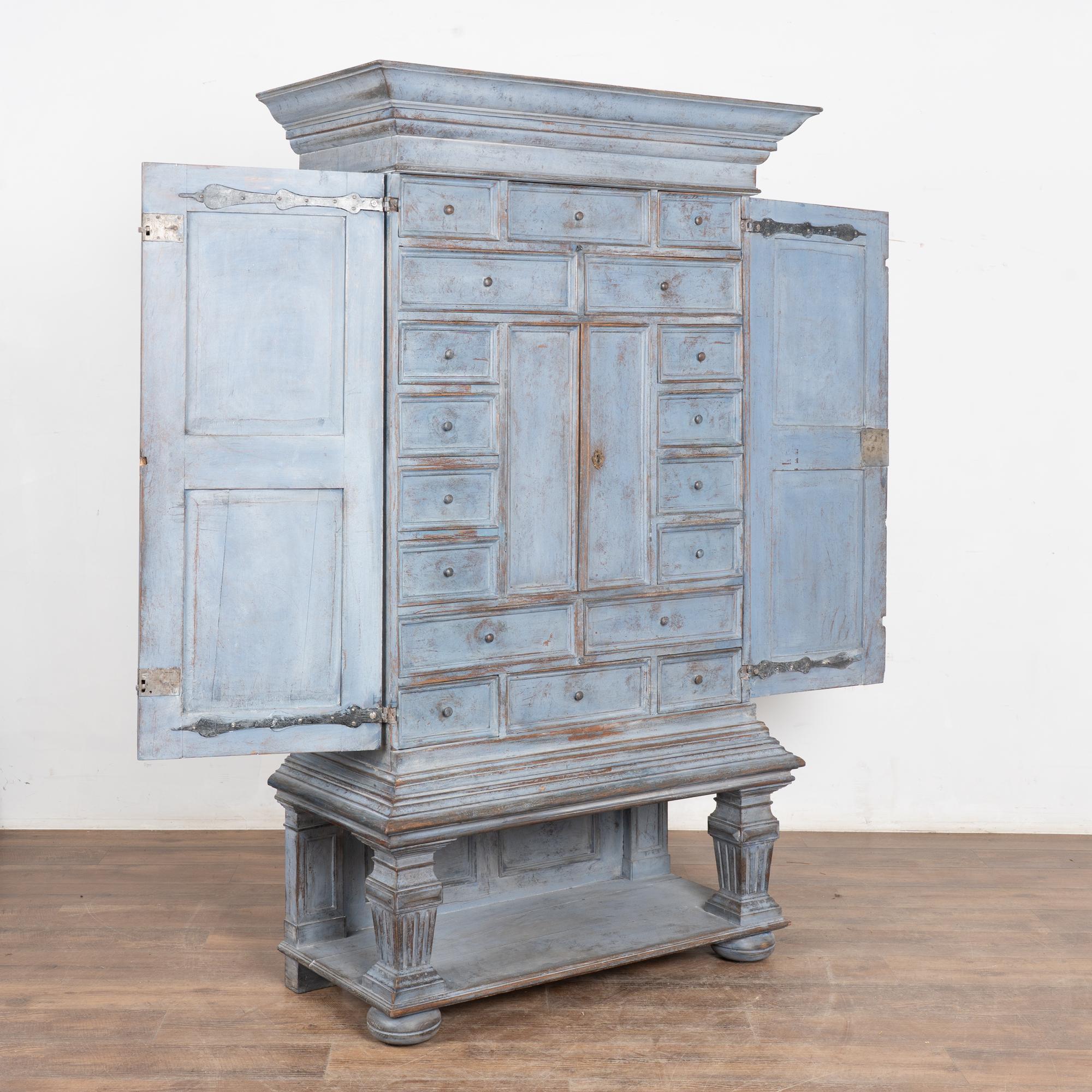 Armadio in pino svedese dei primi anni del 1800, con un'unica sezione superiore chiusa che contiene 18 cassetti e un piccolo armadietto interno.
La nuova finitura verniciata professionalmente di colore blu è stata delicatamente rovinata, rivelando