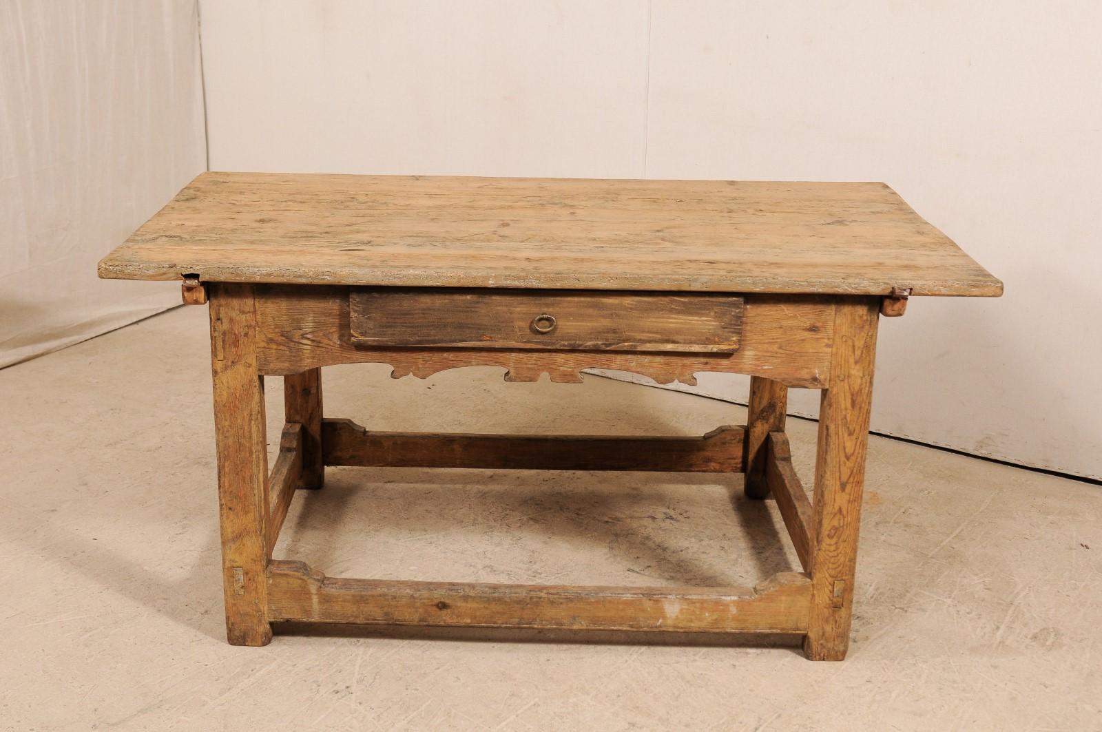 A Swedish desk table with sliding top from the early 19th century. This antique table from Sweden has an overhung, rectangular-shaped top, above a decoratively carved apron which houses a single drawer. The table is raised on four thickly squared