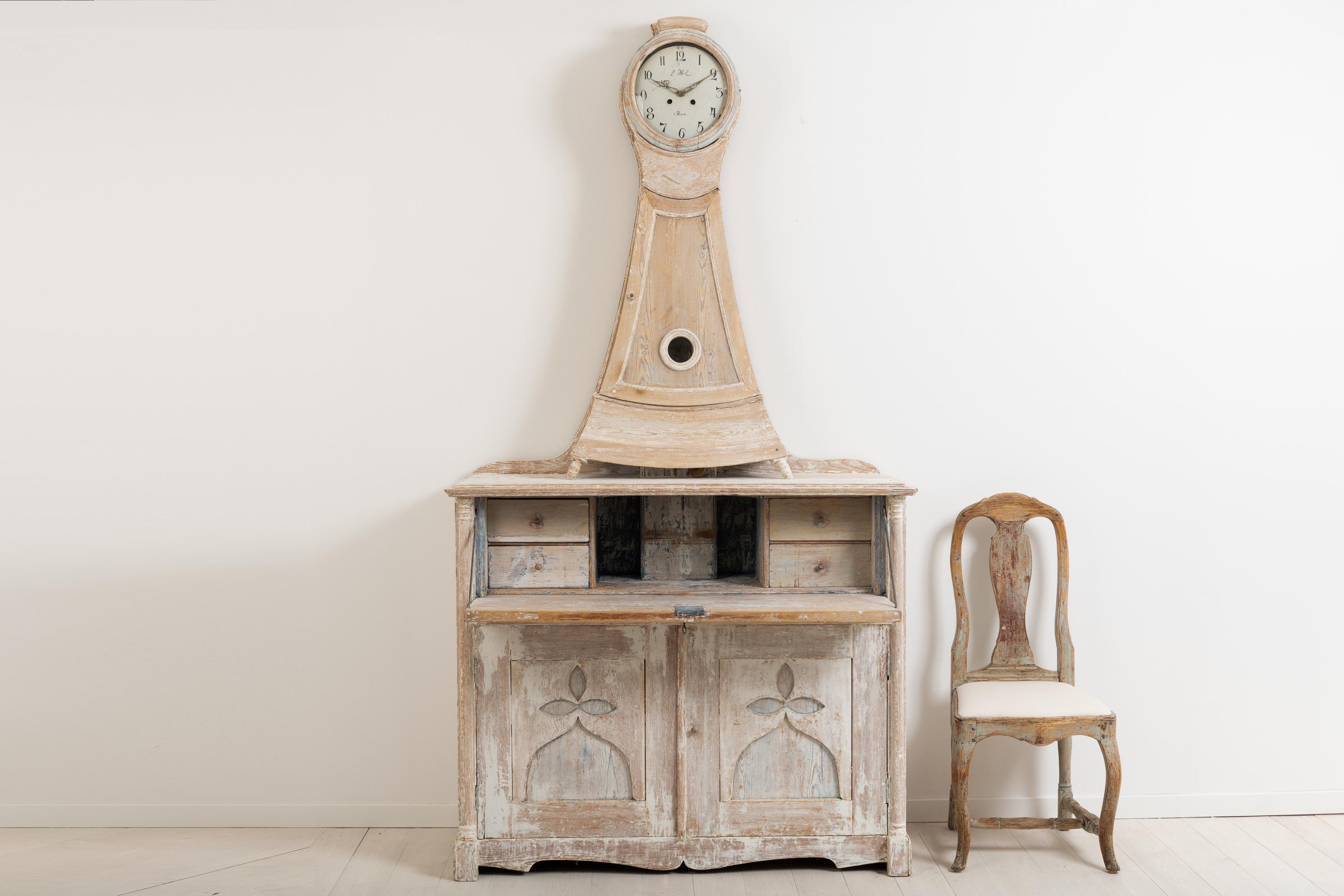 Clock cabinet with a writers flap - a secretary. Manufactured in northern Sweden around 1820 from pine. With traces of original paint. Original working lock and key in the secretary. The cabinet is in two parts. The clock mechanism was working at