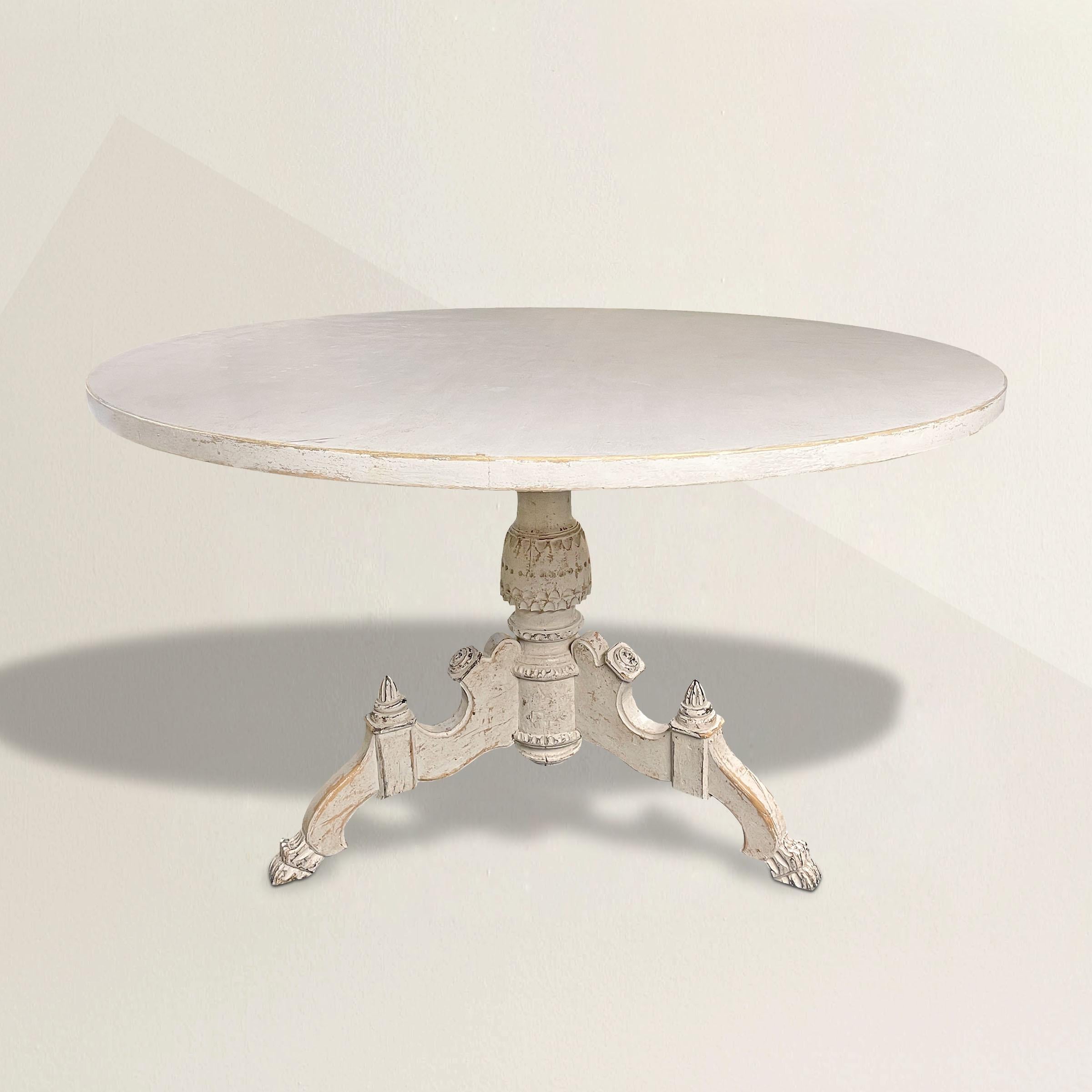A stunning early 19th century Swedish round dining table with an ornately chip-carved pedestal supported by three legs, each with acorn finials, and ending in stylized lion paw feet, and retaining its original white painted surface.