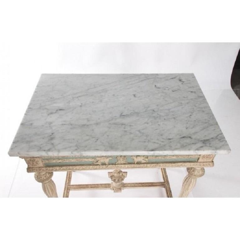 Stunning Gustavian style console table dating to the early 19th century Empire period. Painted white with blue accents, this antique table features a carved scene of mythical griffins guarding a neoclassical urn. Whimsical floral motifs, like