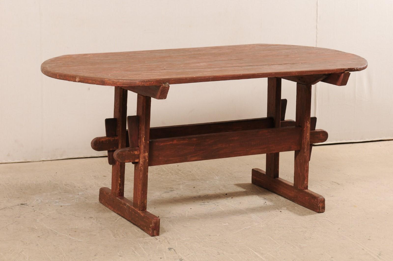 A Swedish falu painted trestle table from the early 19th century. This antique table from Sweden has an overall oval-shaped top (with straight edges at each longer side) which is supported by trestle end supports, and canted wood stretchers down