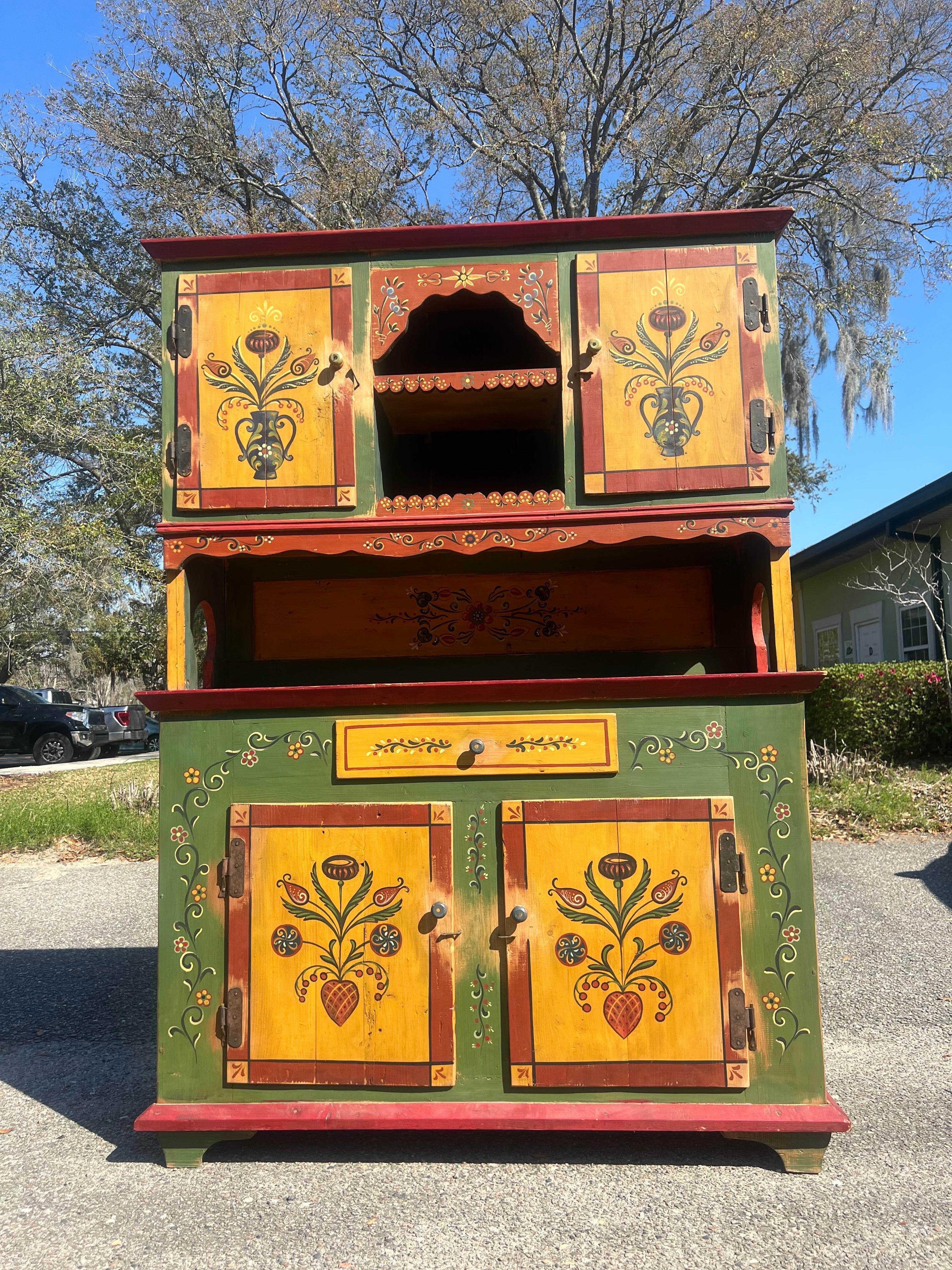 This lovely 2 piece cabinet has a beautiful floral design with the main colors being yellow, green, and a rustic red. The lower portion has 2 doors with a single removable shelf inside. Original hardware throughout the piece. The top with open