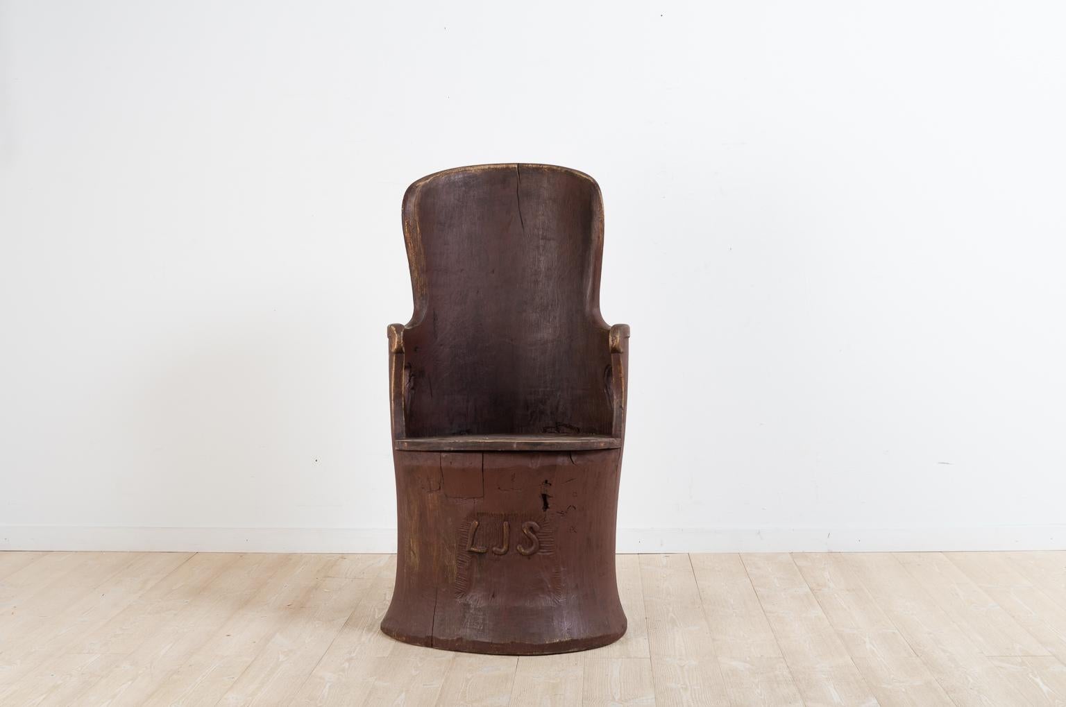 Swedish Folk Art kubbstol manufactured from a hollowed pine trunk. It has a carved monogram under the seat. The armrest on the sides each have a cutout in the shape of a heart. The kubbstol has an older repair under the seat. 

Manufactured in
