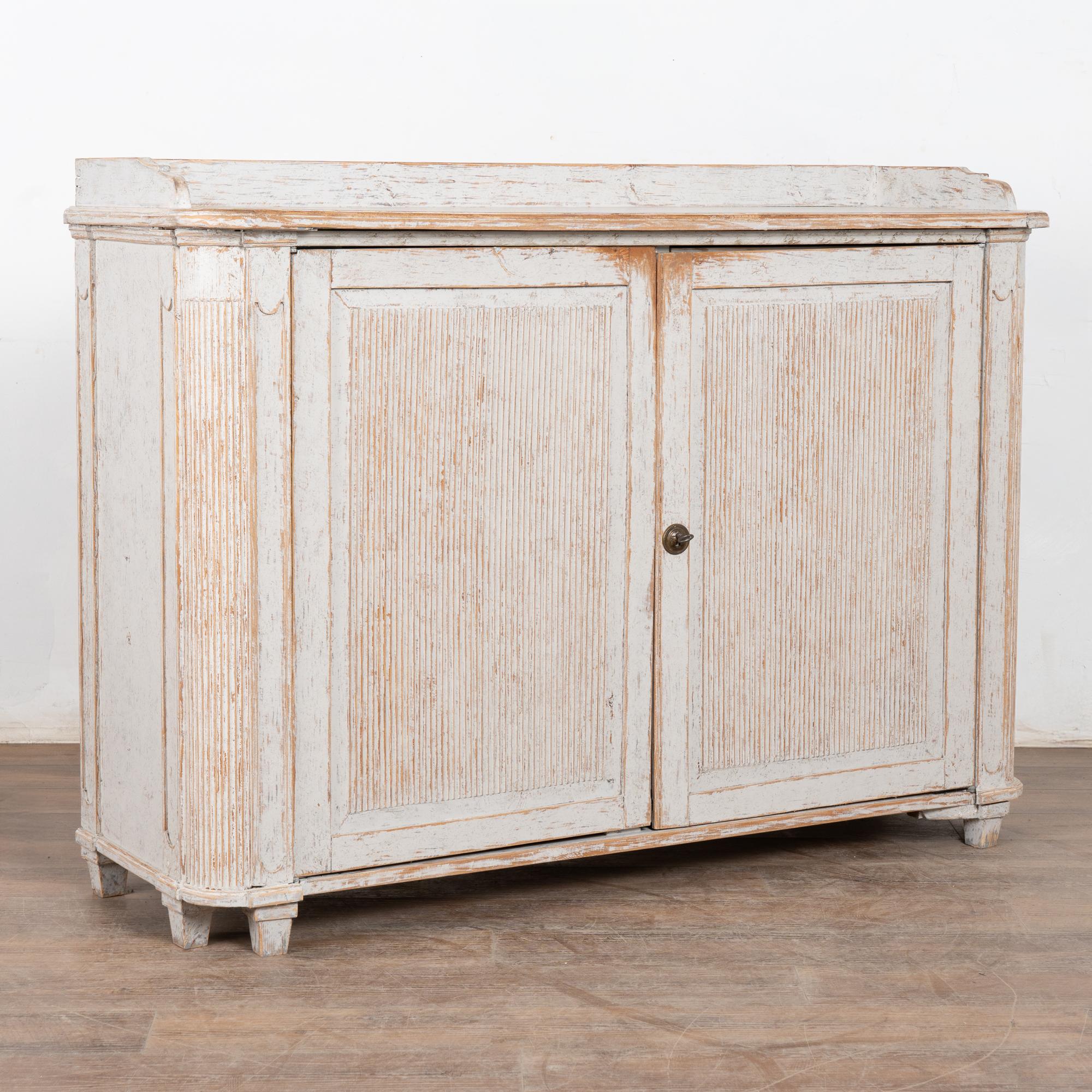 The attractive soft color pallet of this Swedish pine cabinet or sideboard comes from the original hand-painted light gray finish which has been gently scraped and softly distressed through generations of use, resulting in the warm aged patina of
