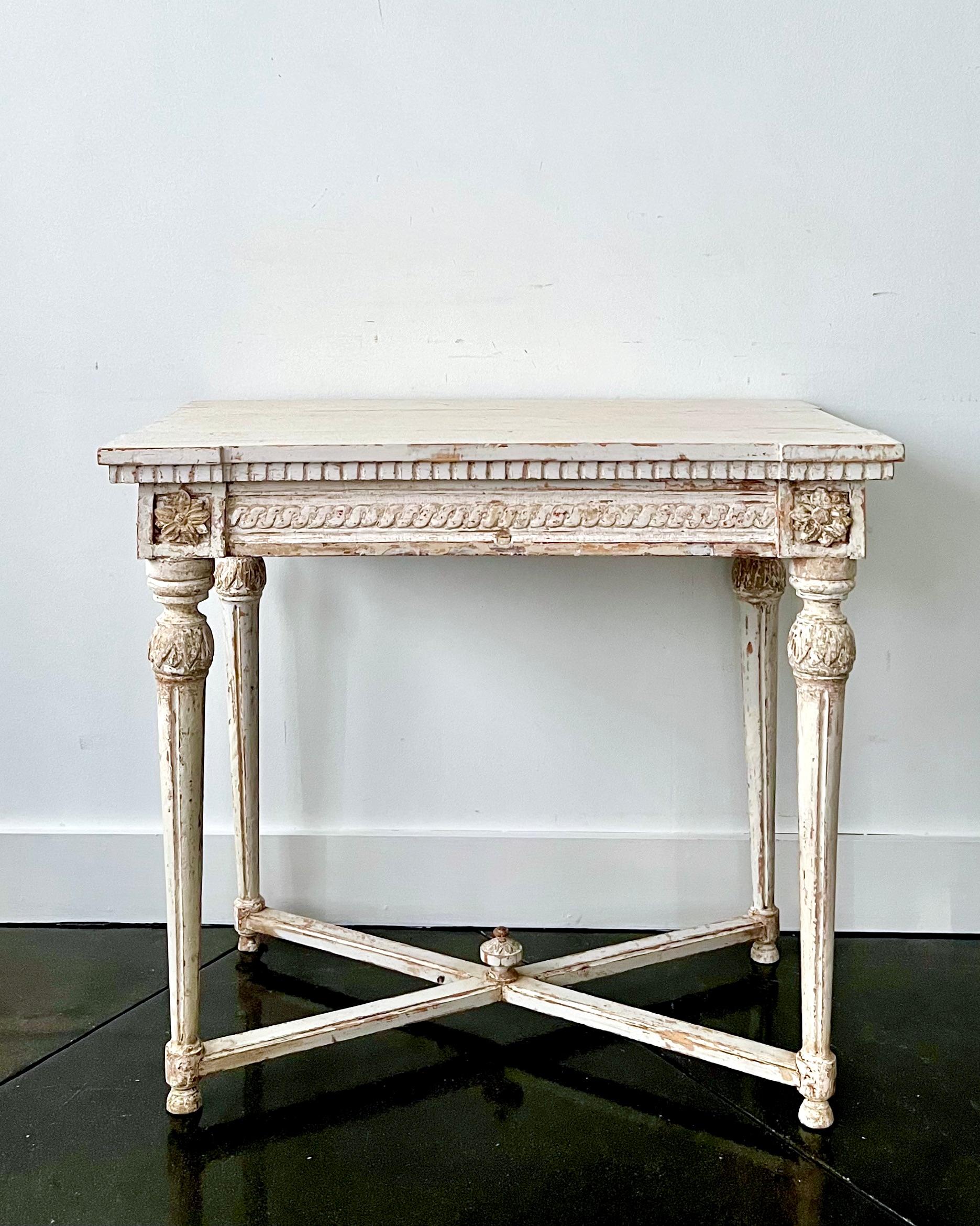 Early 19th century Swedish Gustavian Neoclassical painted console table with very richly carved apron, tapering carved legs and saltire stretcher with central medallion in painted original worn cream patina, Sweden, circa 1820.