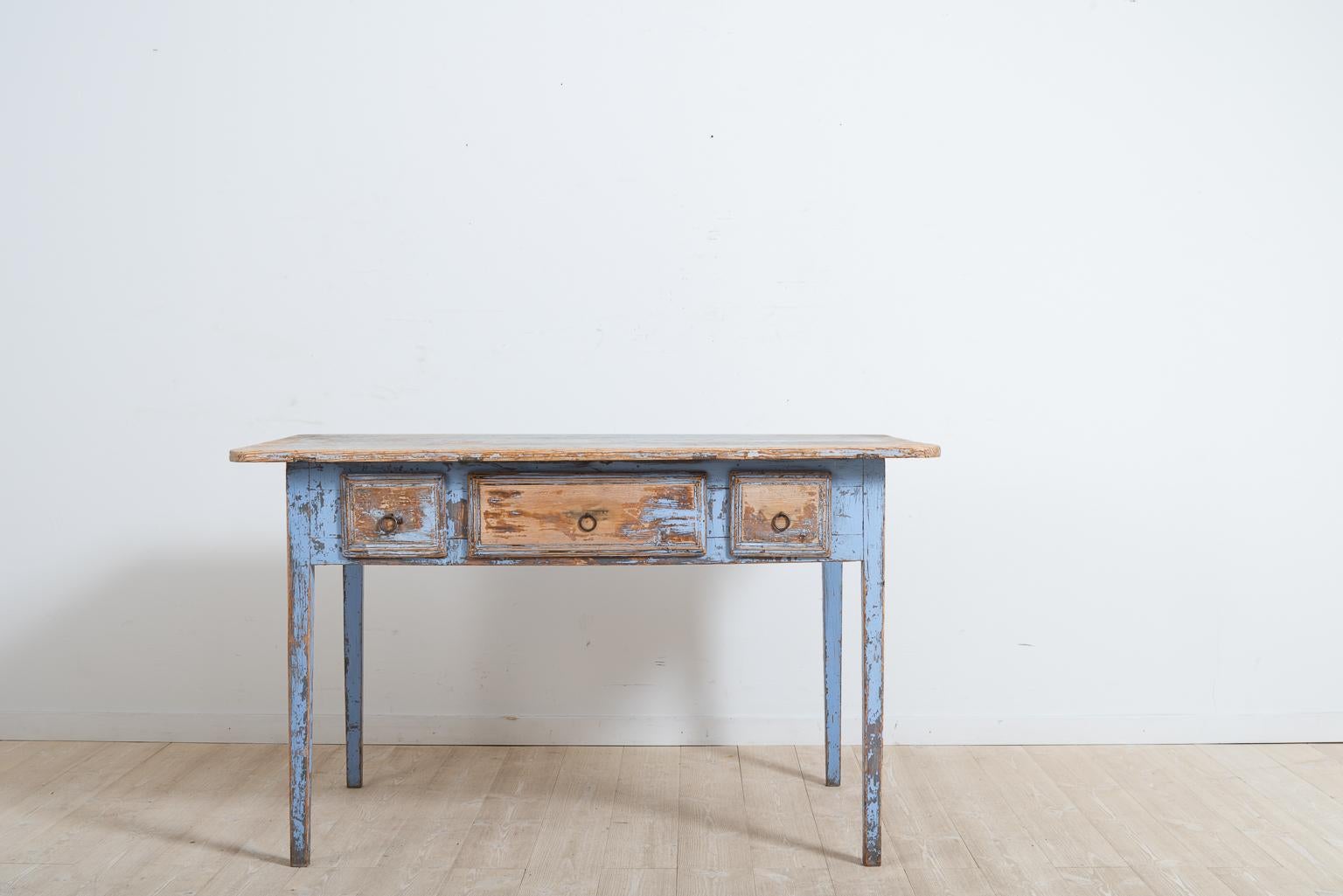 Provincial gustavian table or desk from northern Sweden. The table is made in painted pine and has distressed light blue paint. Made around 1820, the table has straight tapered legs and three drawers. The paint is significantly distressed in places