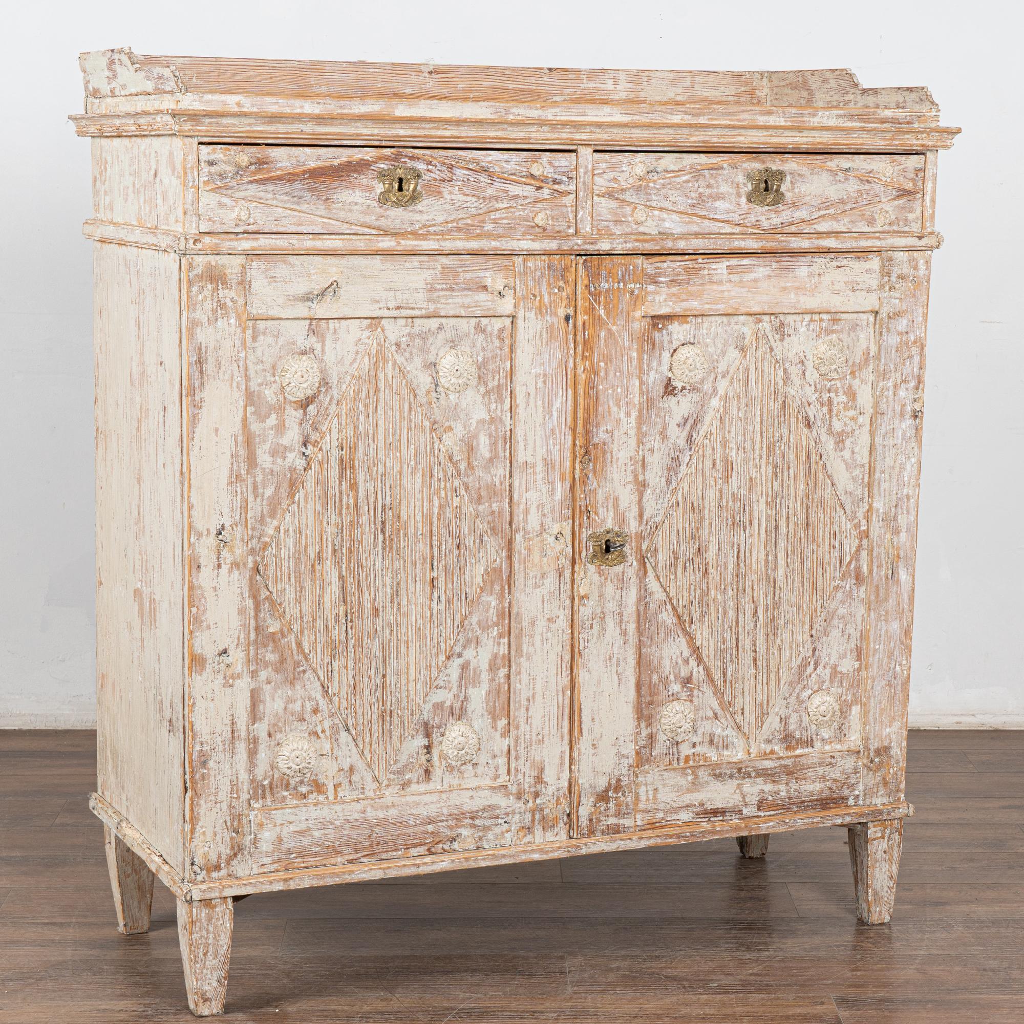 Credenza o mobile server originale gustaviano in pino dipinto di bianco con tradizionali pannelli a diamante scanalati intagliati nelle porte, piedi affusolati.
La finitura originale verniciata di bianco è stata delicatamente raschiata, rivelando il