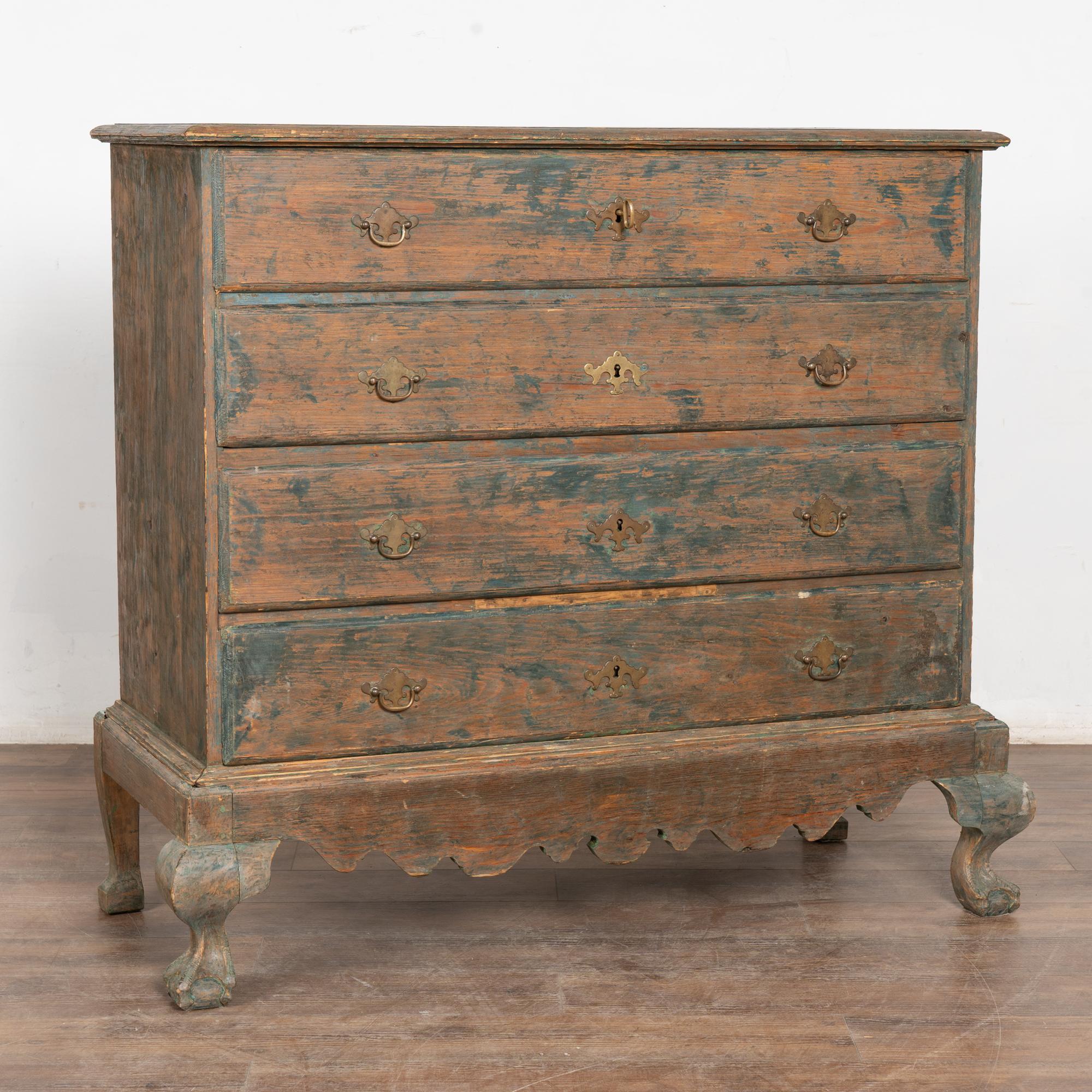 Gran cómoda original de pino pintado de verde azulado con cuatro cajones y faldón festoneado, todo ello apoyado sobre patas de bola y garra cabriolé.
El acabado original pintado de azul/verde se ha raspado y frotado, revelando la pátina de pino