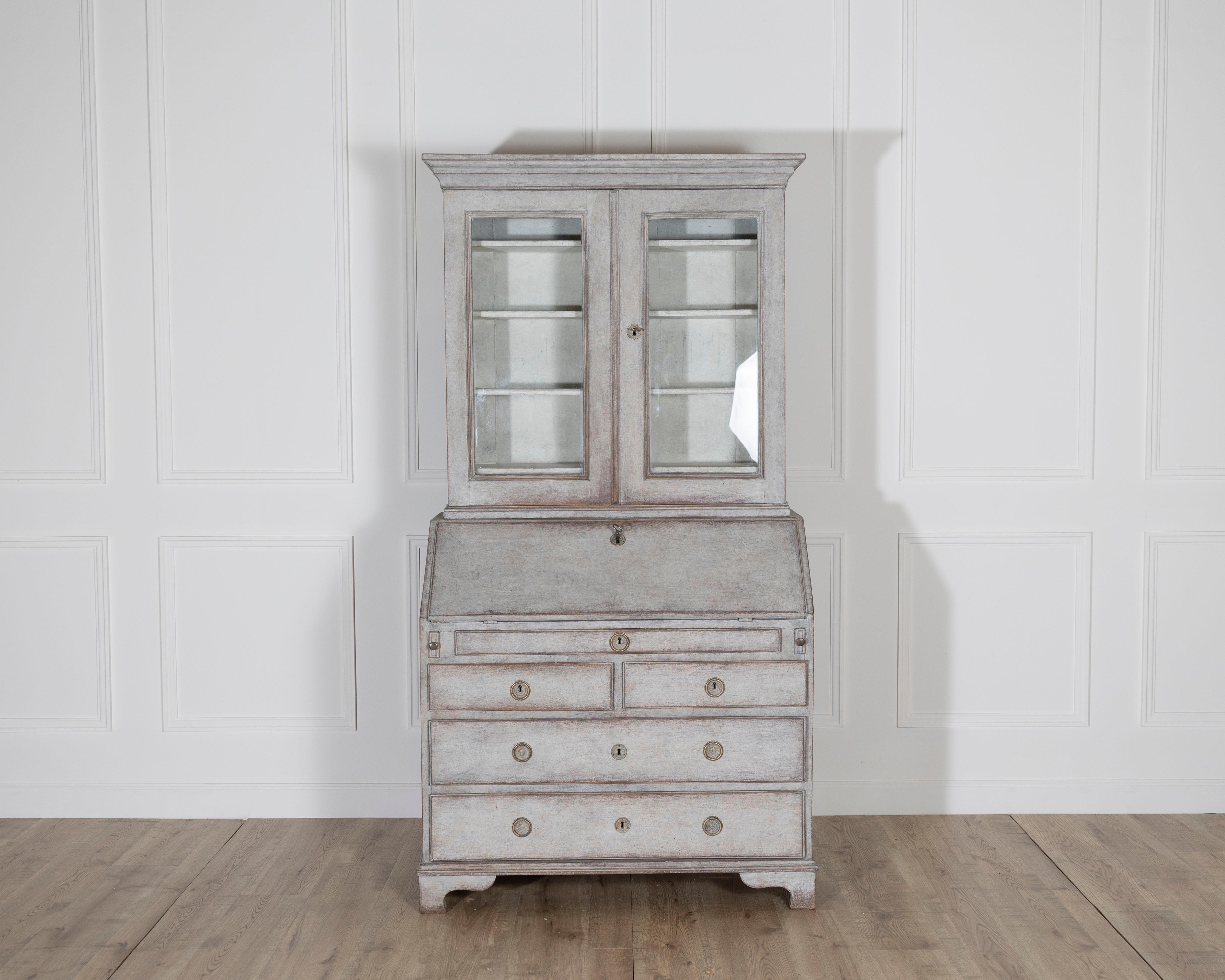 Excepcional armario de secretaria sueco de principios del siglo XIX, circa 1810-1830, acabado en gris suave con una hermosa pátina envejecida. Fabricada en roble y pino, la construcción en dos partes incluye un armario superior acristalado con tres