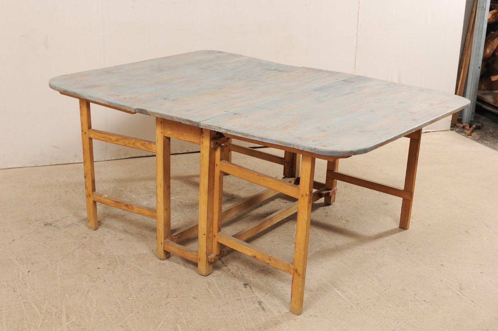 A Swedish painted-wood table with gate legs from the early 19th century. This antique table from Sweden features clean, simple lines, a painted wood top with rounded corners with two nicely-sized drop leaves. The table is supported with a