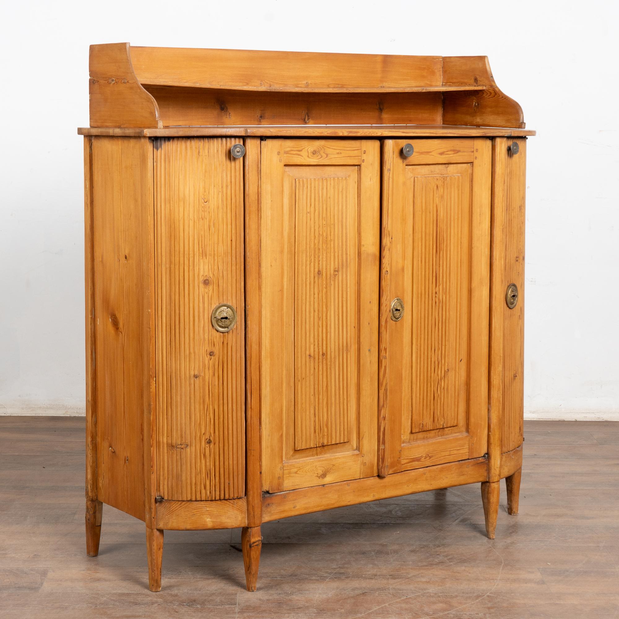 Credenza in pino svedese dell'inizio del XIX secolo con piedi affusolati e finitura a cera naturale che mette in risalto il tono caldo del pino. L'interno e il retro sono stati verniciati in un secondo momento con una finitura bianca e distorta.
Le
