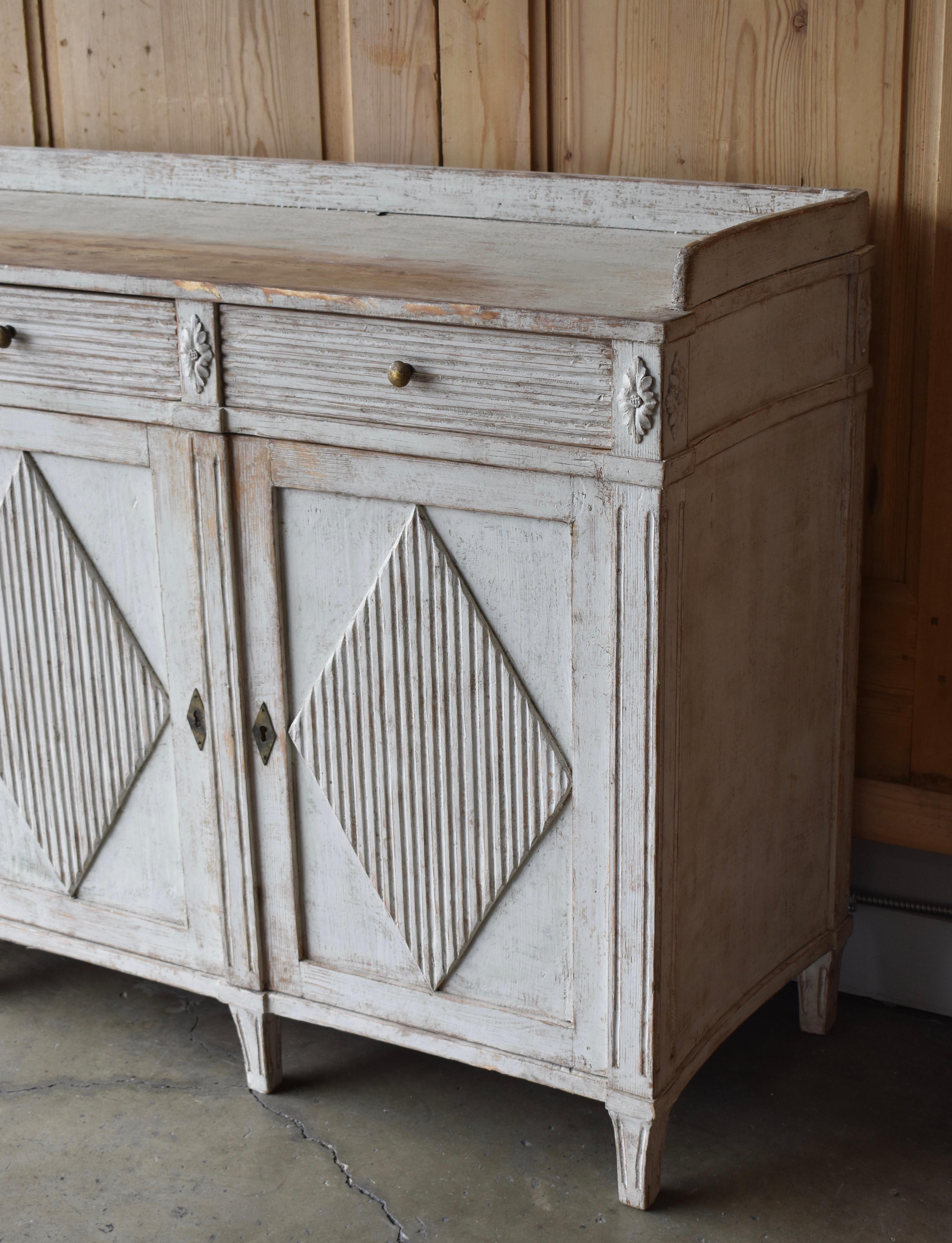 Early 19th century Swedish Gustavian style painted three door sideboard. Beautiful curved sides with wonderful three hand-carved drawers over three reeded front paneled doors. Each door is adorned with a diamond pattern. The top is surrounded with a