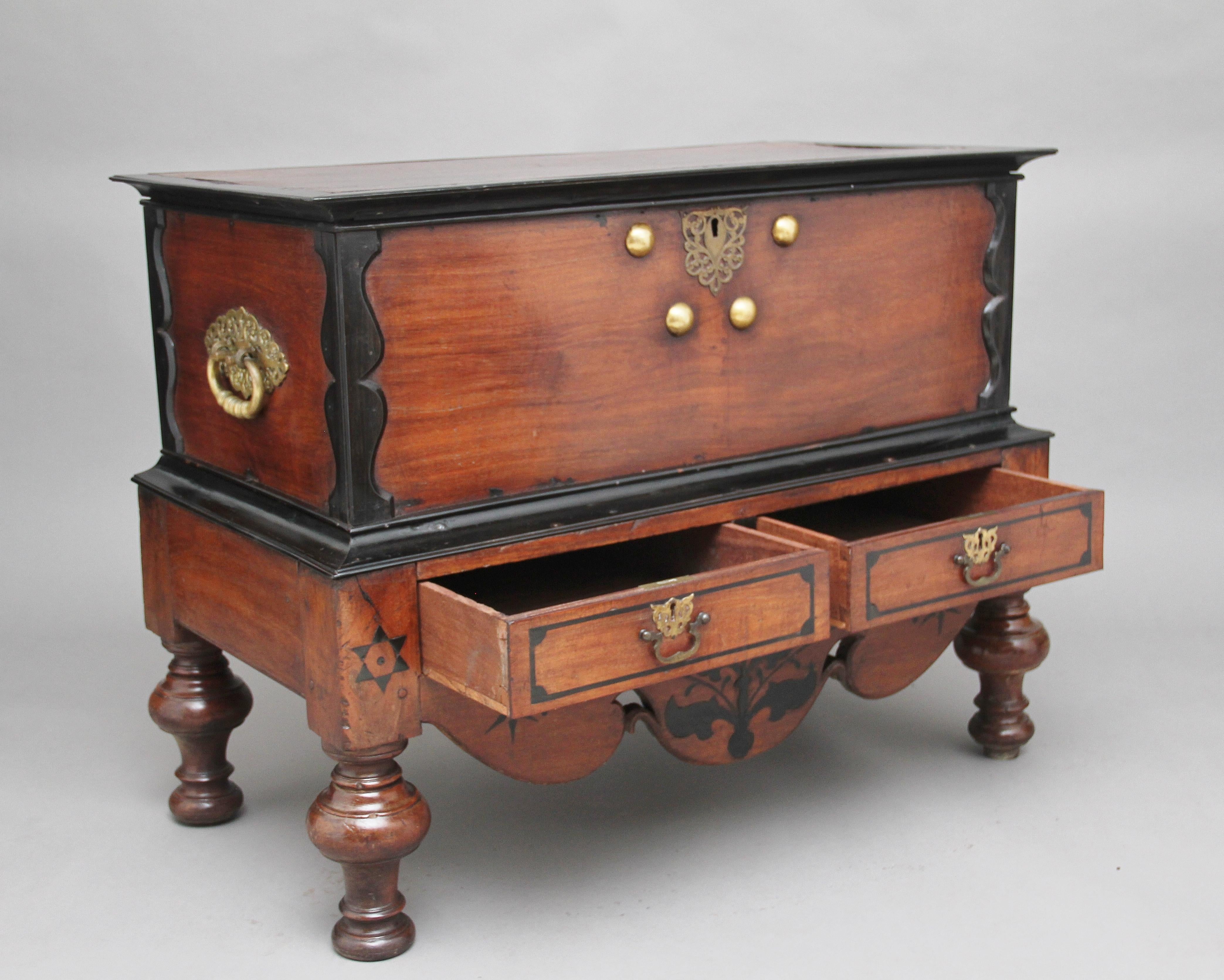 Early 19th century Ceylonese teak and ebony chest / coffer, the hinged lift up top, with ebony moulding, opening to reveal a large compartment space, the outside of the top sections having original brass carrying handles to the sides and brass stud