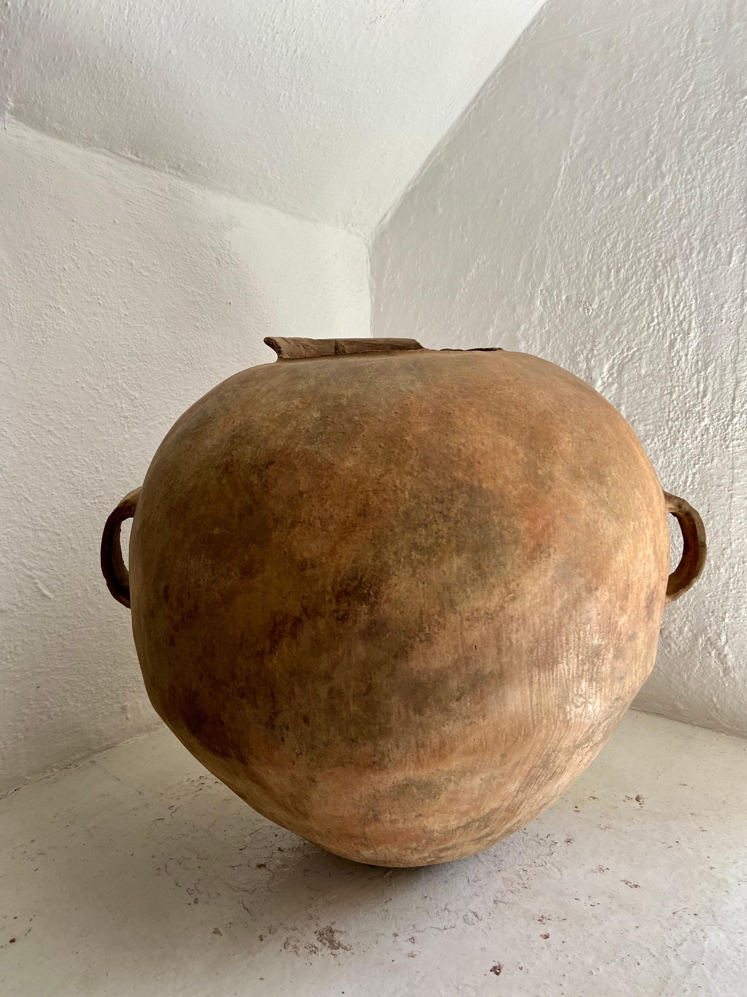 Early 19th century terracotta water jar from Norther Puebla, Mexico. Unusually wide format pot with large intact handles. The majority of the neck rim has been broken off through time. The pot has a warm, muted orange color.