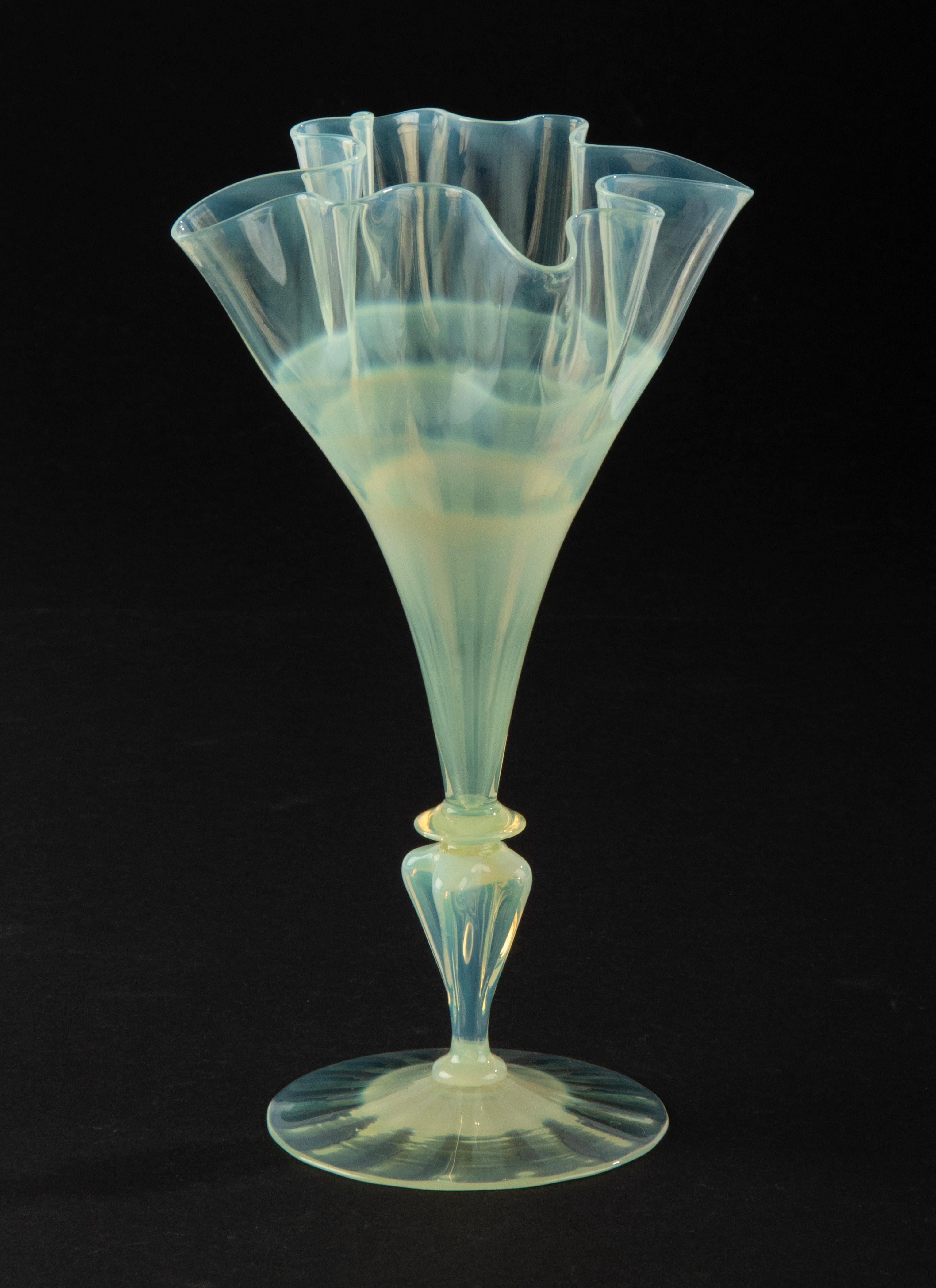 Un petit vase en verre, fabriqué à la main à partir de verre fin, avec un calice exubérant en forme d'éventail. Une belle pièce d'artisanat. Le vase a une couleur spéciale, jaune clair / vert, probablement une petite quantité d'uranium a été ajoutée