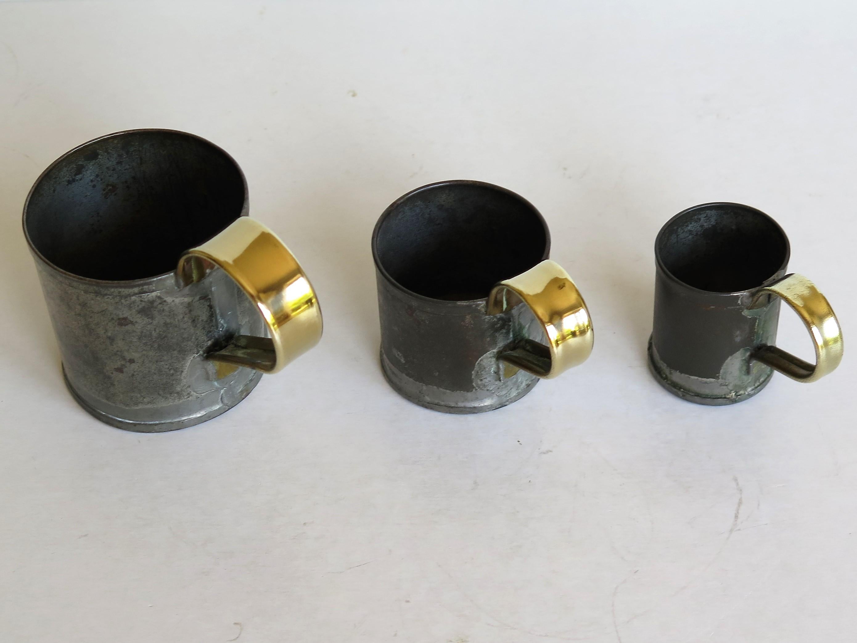 These are a good graduated set of three Gill measuring cups as used in Ale houses in 19th century, England. 

The measures are handmade of tin with soldered joints and high loop brass handles.

Each cup is impressed with its capacity; Gill, 1/2