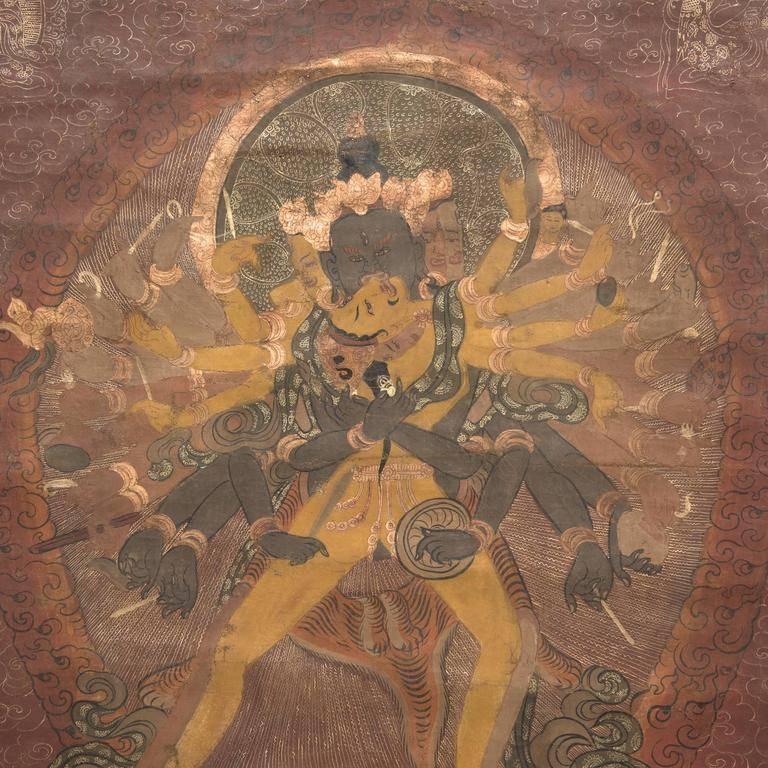 The rich orange, red, green, and blue hues are still incredibly vibrant in this sacred Tibetan thangka painting. At this centre is the figure of an important multi-armed deity called Chakrasamvara seated on a lotus blossom throne. The painting is