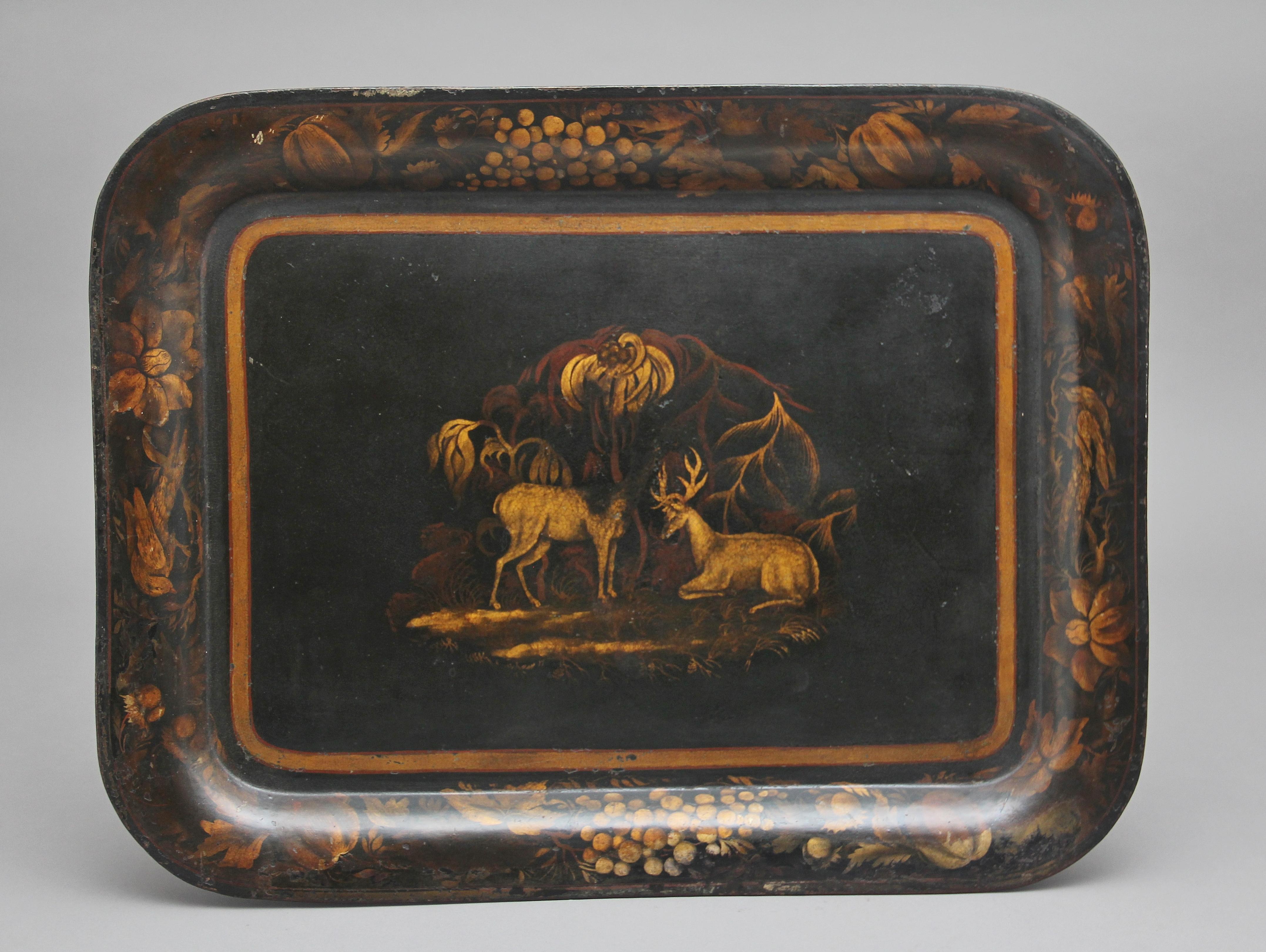 Early 19th century toleware tray on later stand, the rounded rectangular serving tray decorated in tones of gilt with stags, within a border of fruiting vine, supported on a mock bamboo base with a cross stretcher, circa 1830.