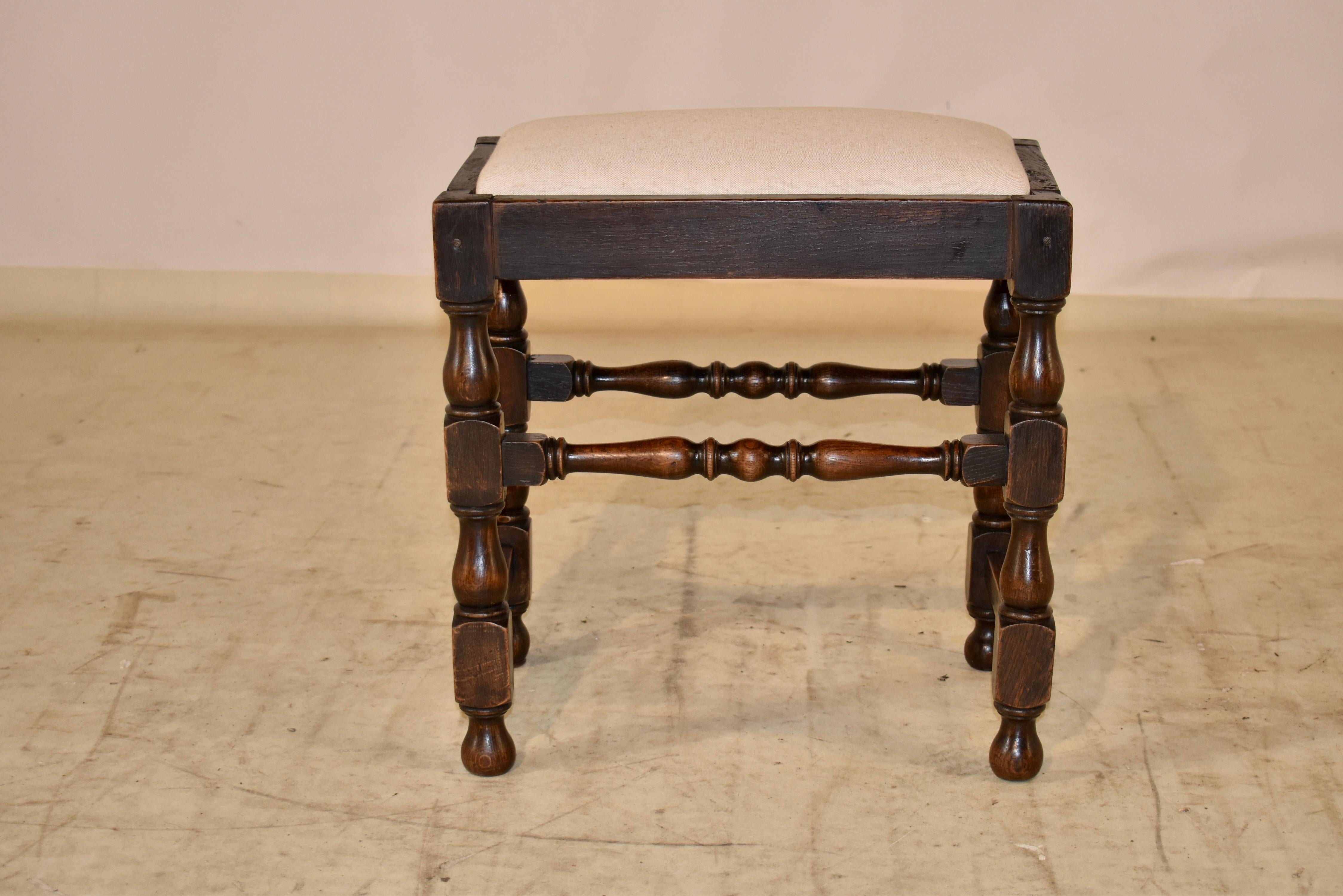 Early 19th century oak stool from England with a newly upholstered seat in linen. The frame is lovely and is supported on hand turned legs, joined by simple stretchers on the sides and complementing hand turned stretchers on the front and back of