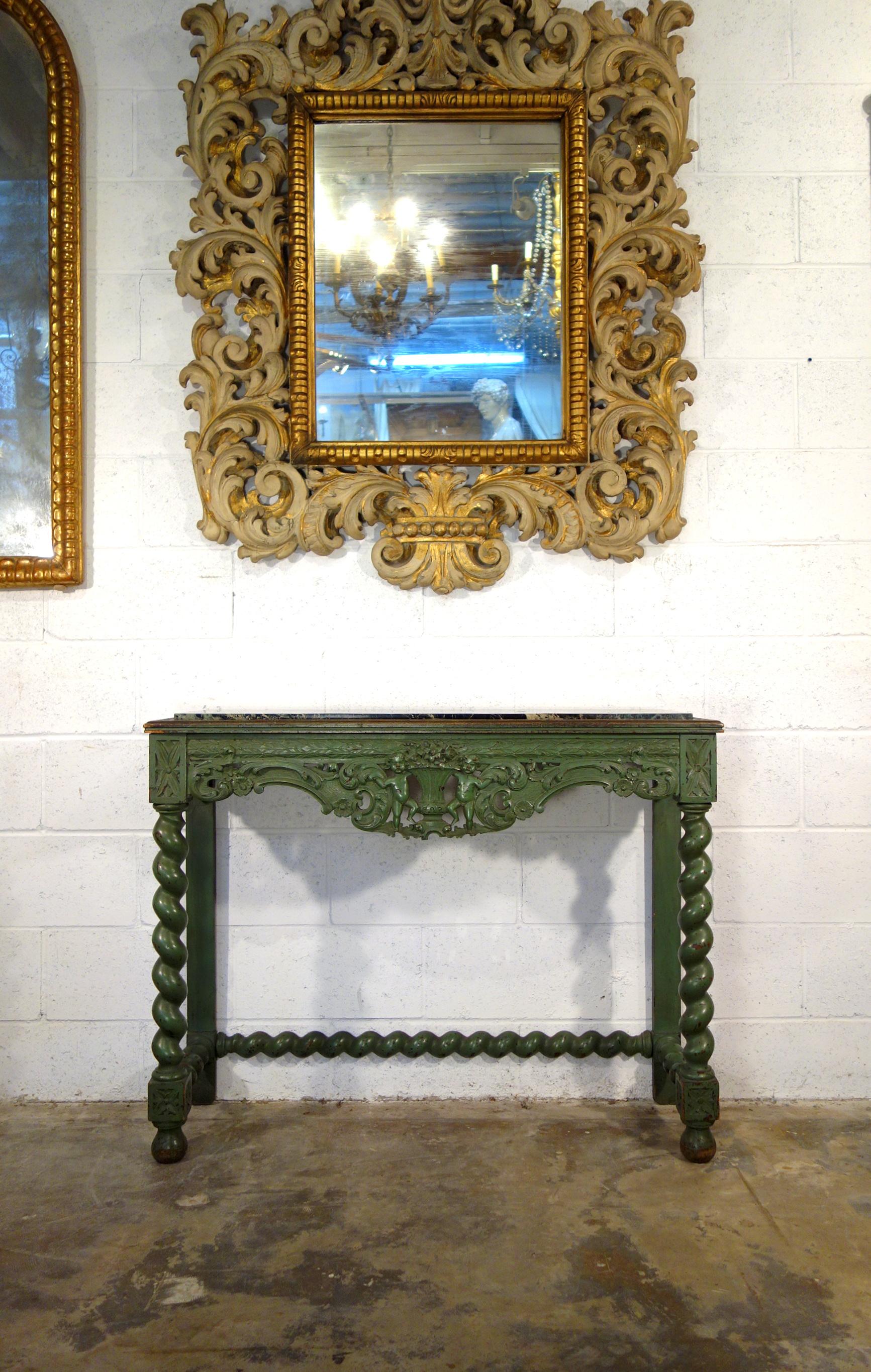 Lovely early 19th century carved console with turned legs and cross stretcher. Two cherubs sustaining a triumph of flowers in the center. Framed inset top is a beautiful piece of deep green marble, possibly Italian Verdi Alpi. 

Measures: 41.75