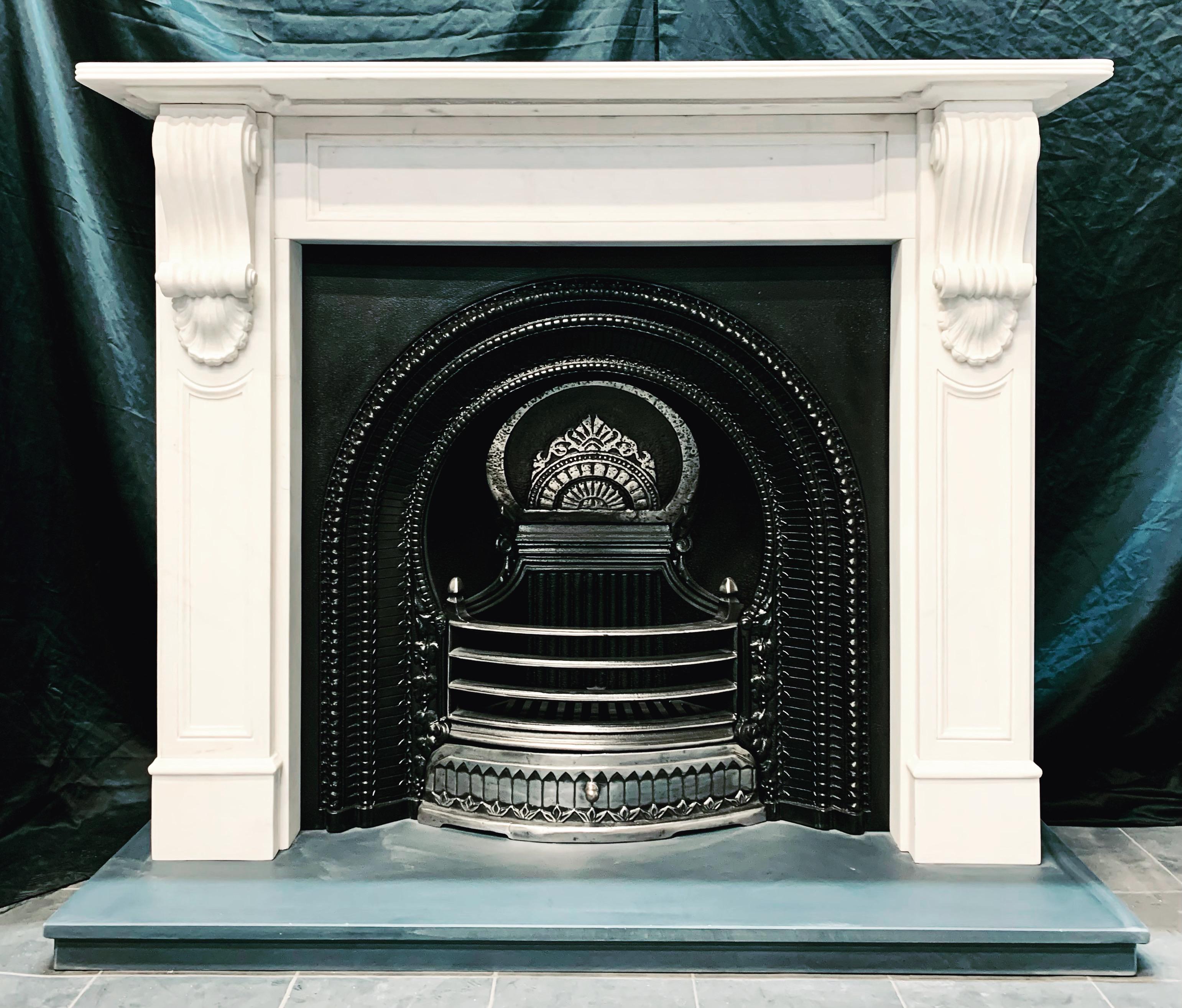 A small early 19th century Victorian manner carved statuary marble fireplace surround. A reeded top shelf sits above a recessed panelled frieze, flanked by jambs with further panelling, jambs are adorned with well carved high relief corbels all