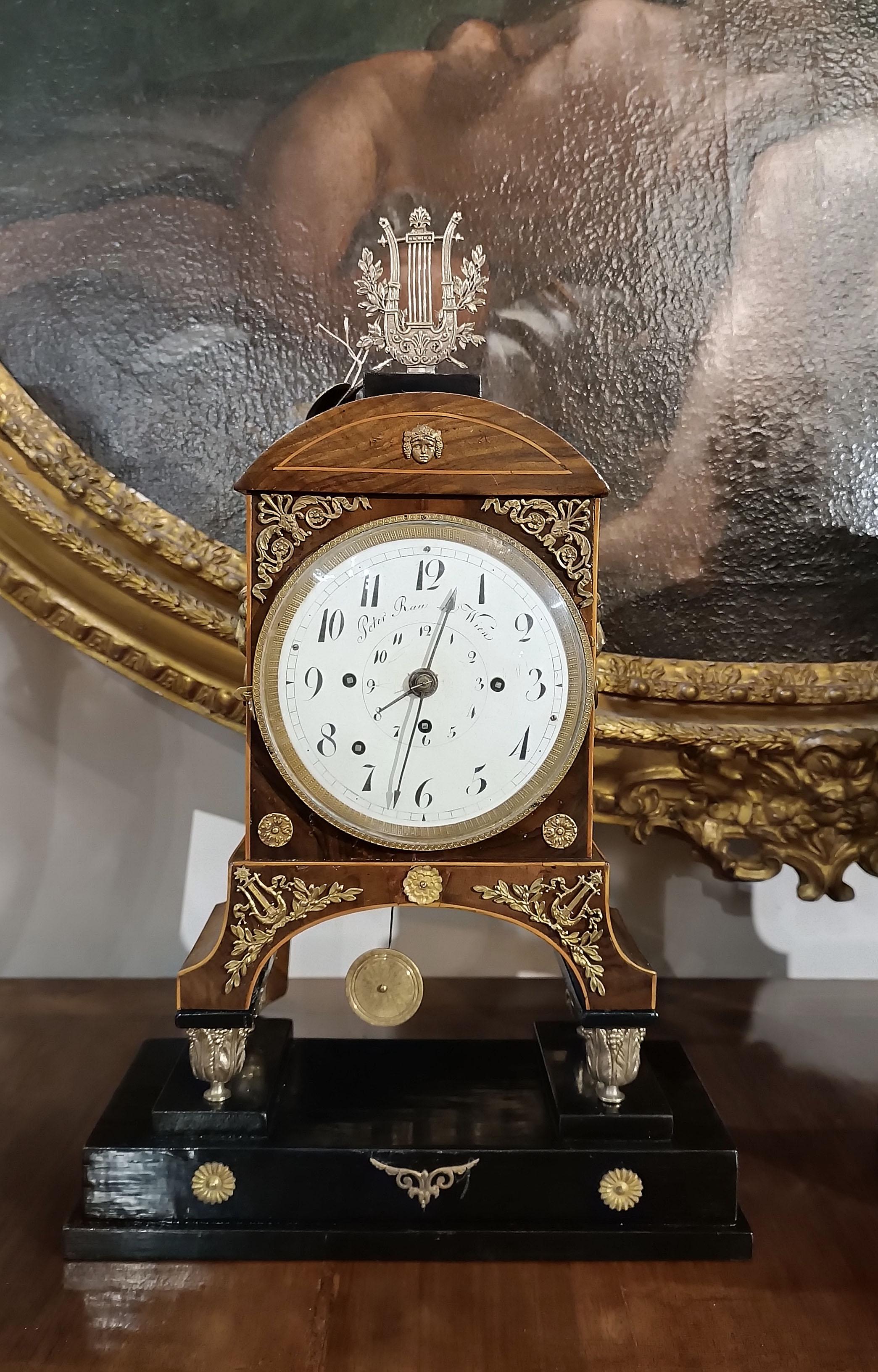 Beautiful clock in walnut root, enriched with maple fillets and with an ebonized wooden base. The decoration of the clock features gilded bronze friezes, inspired by classical elements such as the head of Medusa and the harp, together with refined