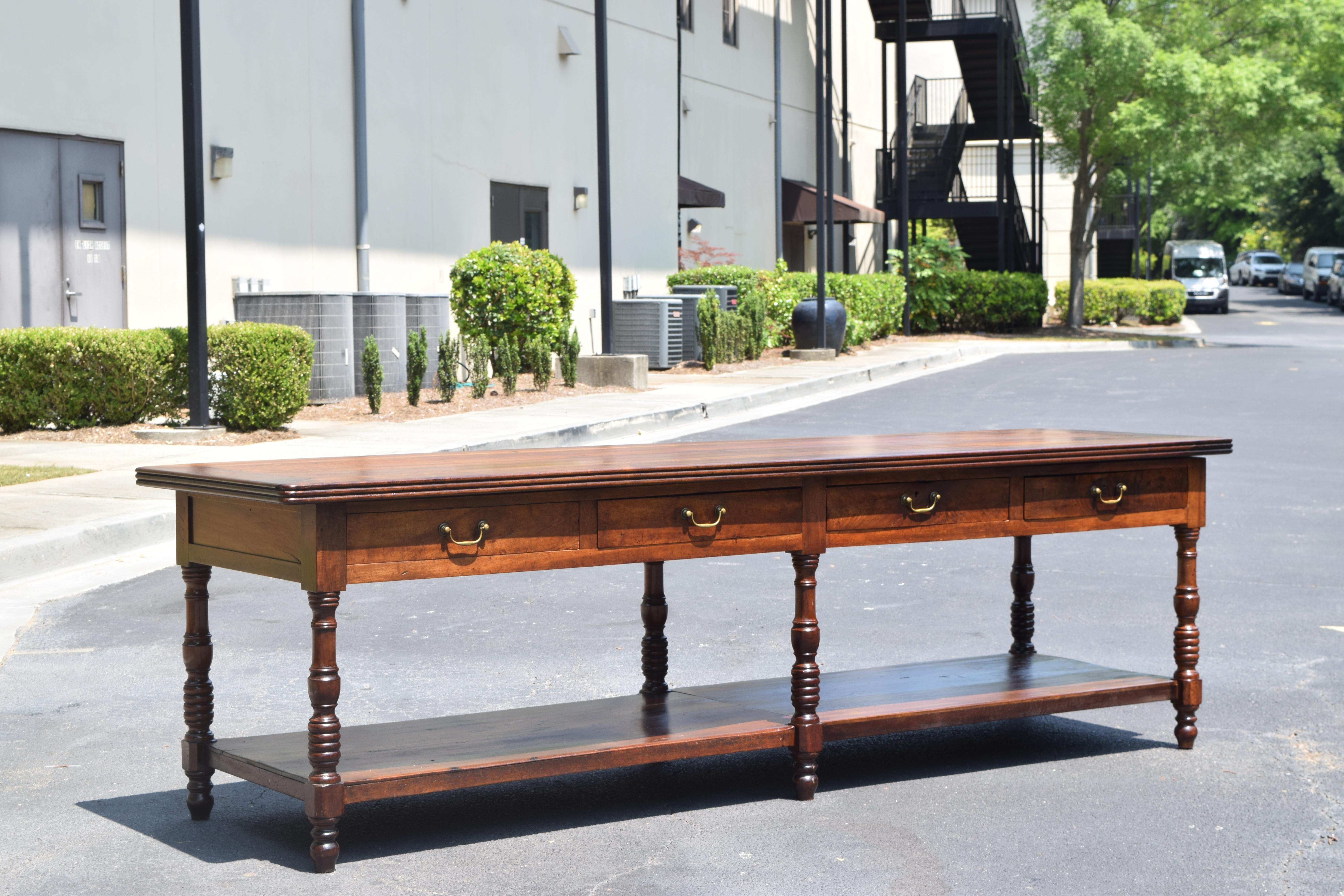 constructed entirely of beautifully grained light walnu this shaped and carved drapers table has four drawers retaining antique bronze handles, with a lower shelf used to hold bolts of fabric and acting as a stretcher for the six turned legs,