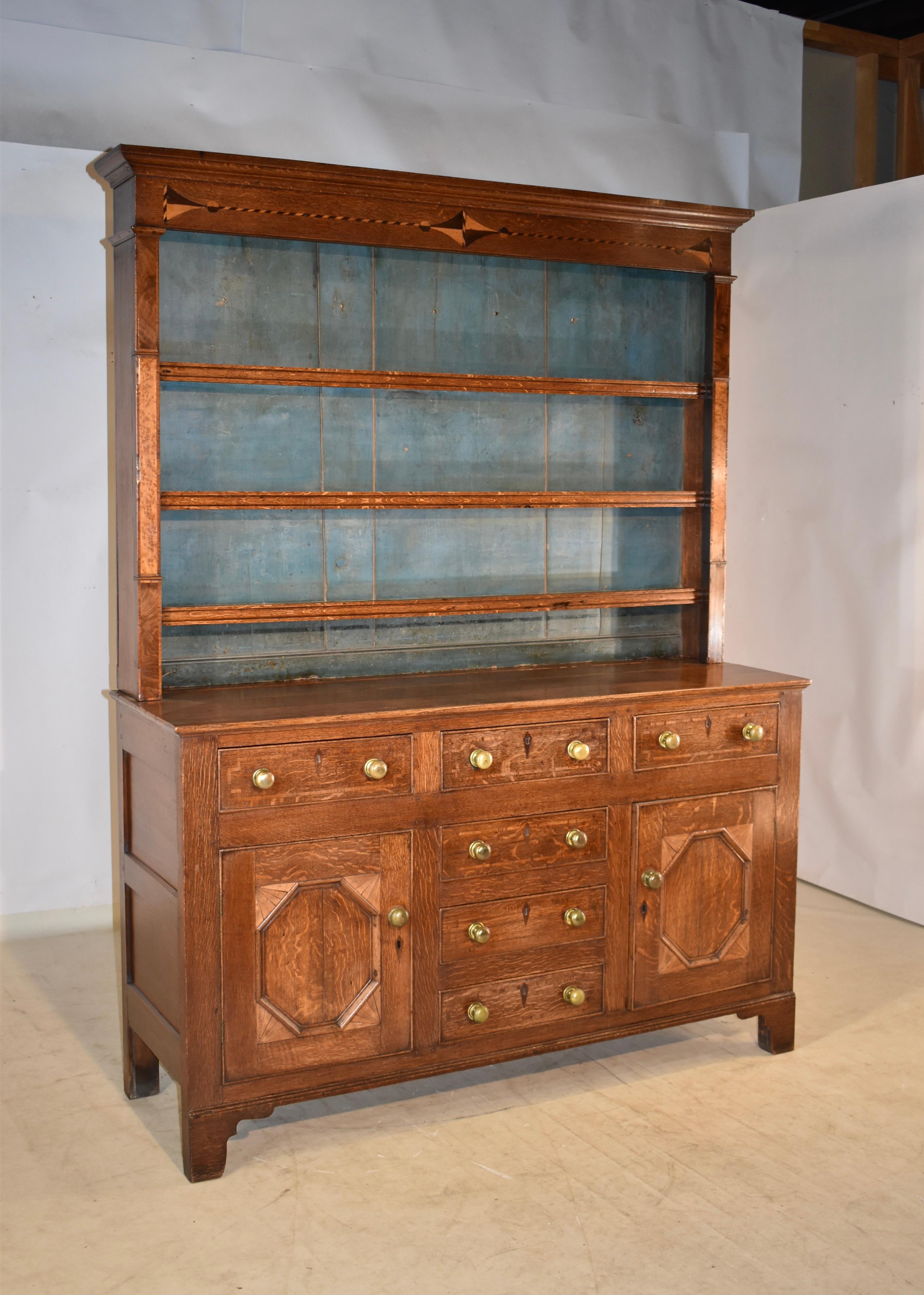 Early 19th century inlaid Welsh oak dresser. The dresser has a lovely and simple crown over a wonderful top with decorative inlay design. The top has three shelve, flanked by sides made from mahogany and bird's eye maple accents. The back boards are